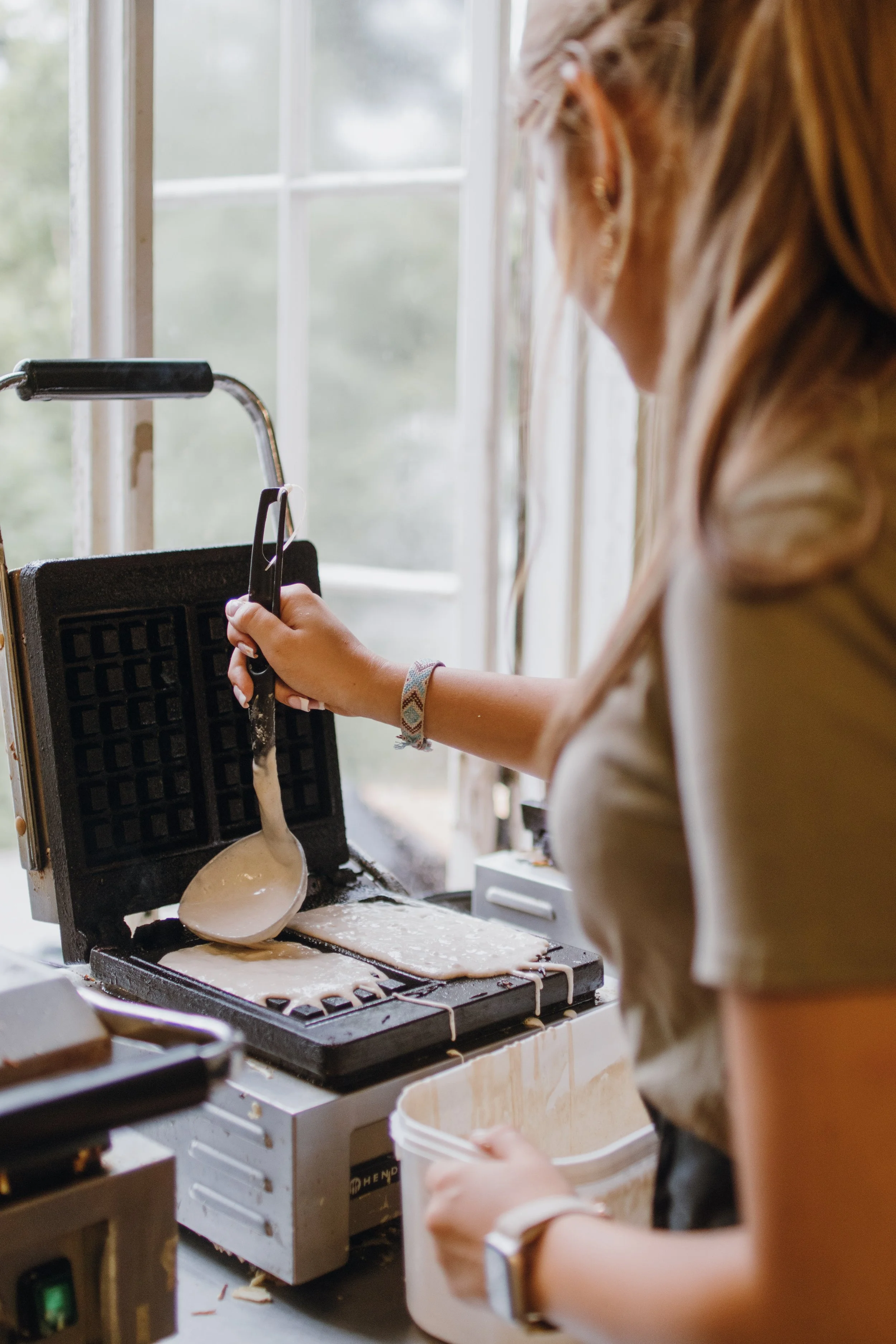 En person som gör våfflor i ett våffeljärn, fyller på smet med en sked.