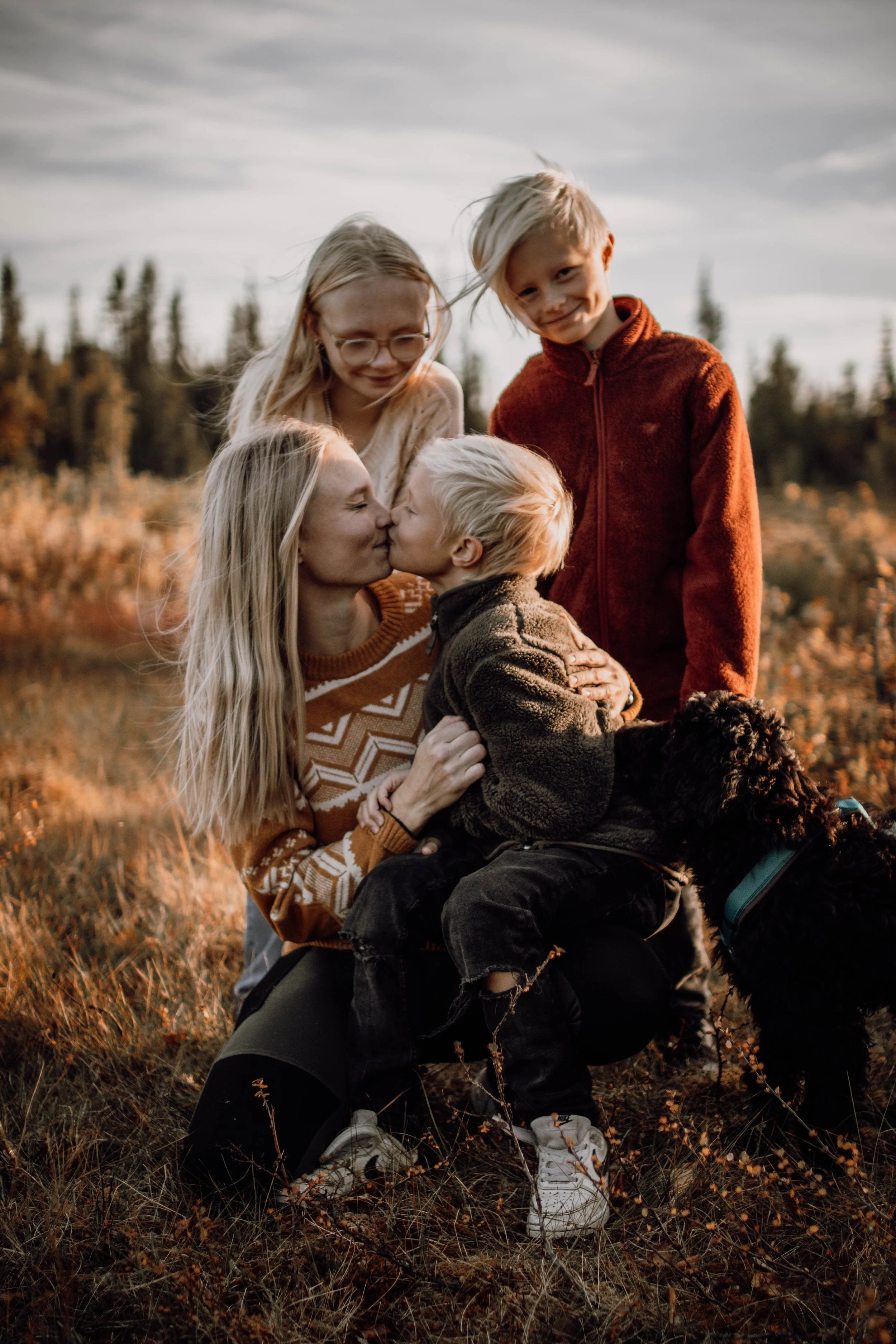 en bild på en mamma med sina två söner och en dotter, den yngsta sitter i hennes knä och de pussas