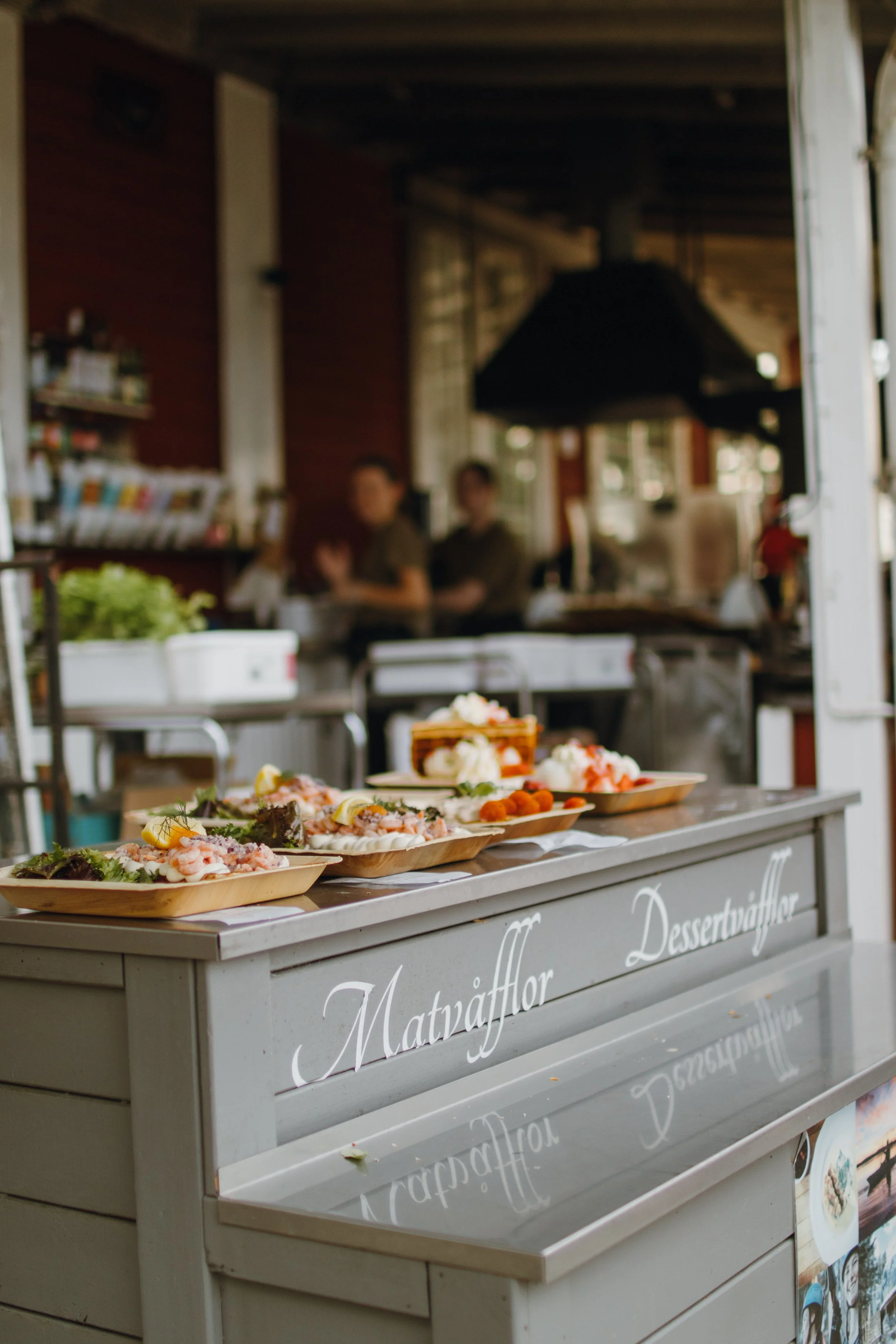 Lagrad mat och desserter på en serveringsvagn utomhus, med personal i bakgrunden, svensk text på sidansidan.