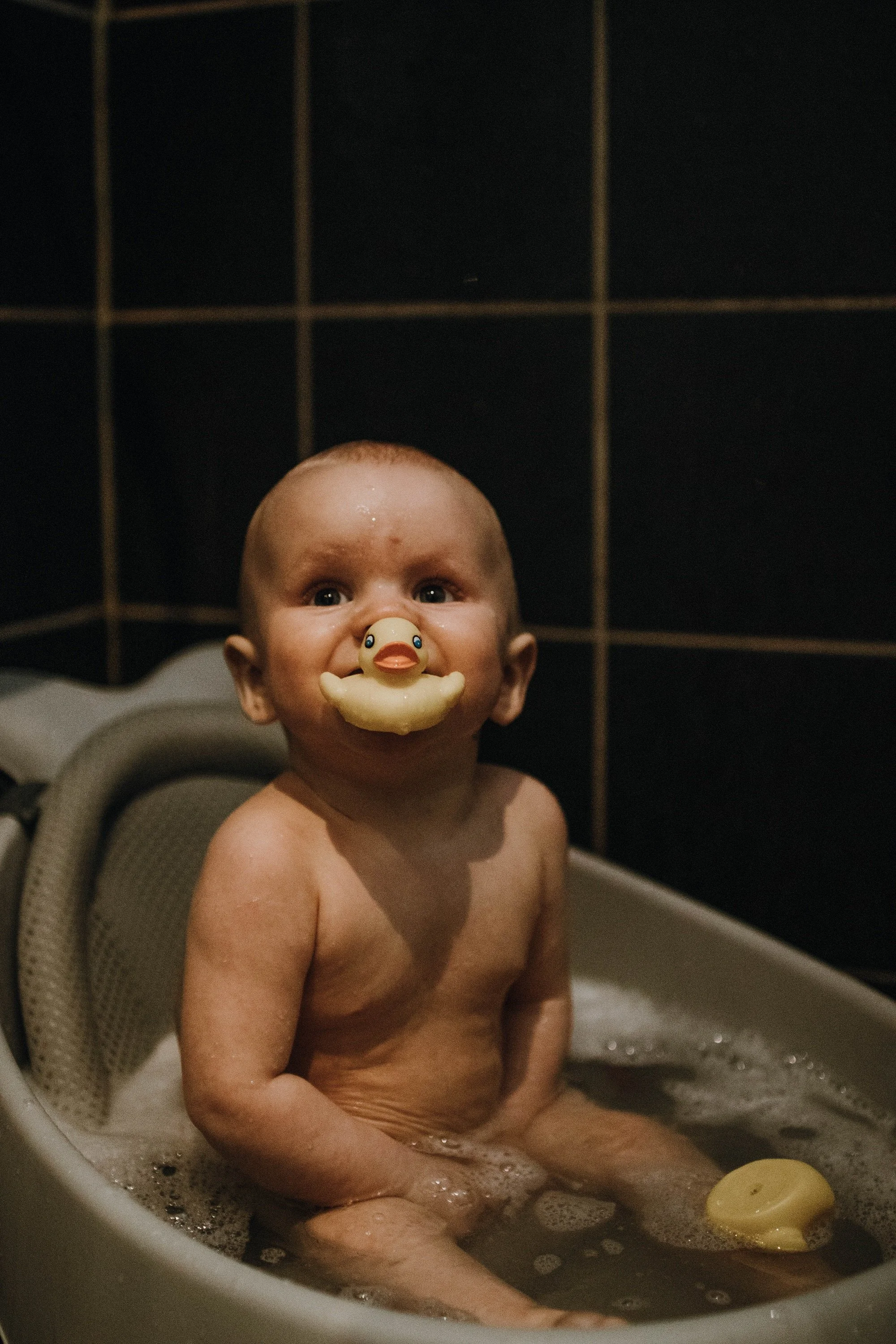 Liten pojke sitter i badet med en gummianka i munnen