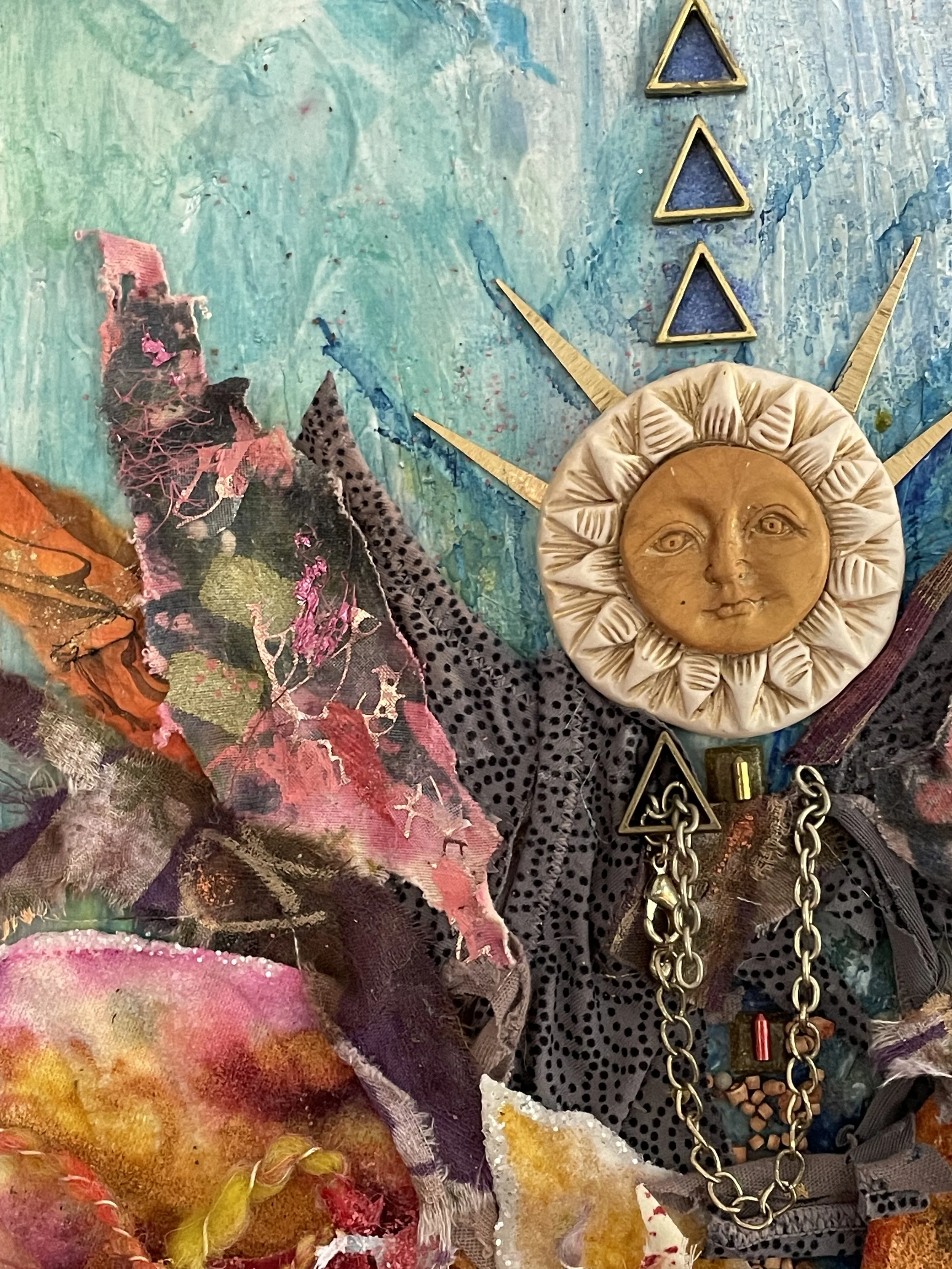 Mixed media art piece featuring a sun face sculpture with a human face, surrounded by colorful fabric, chains, and geometric shapes on a painted background.
