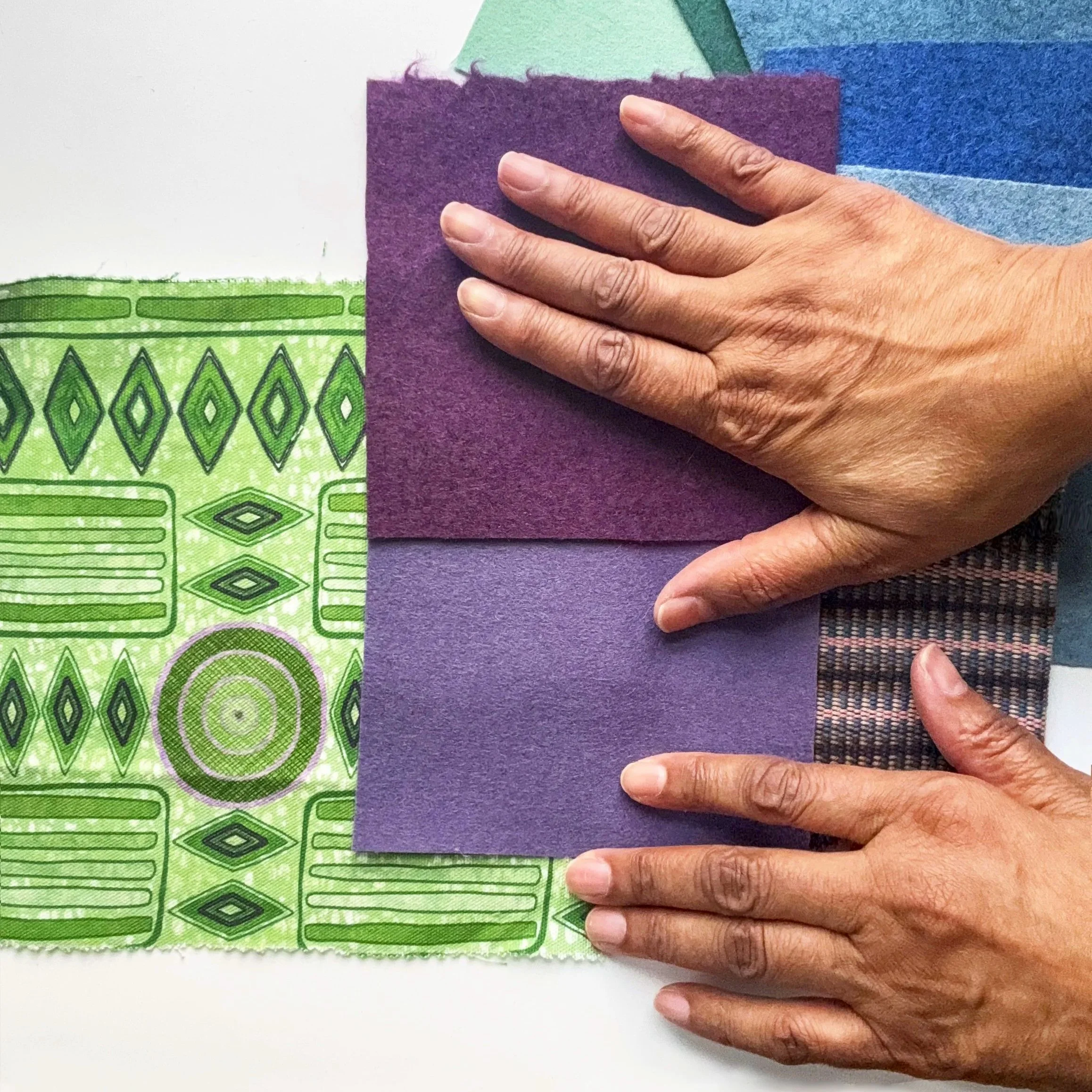 Upholsterer holding a purple felt square over colorful fabric with green, blue, and purple patterns for a fabric consultation.