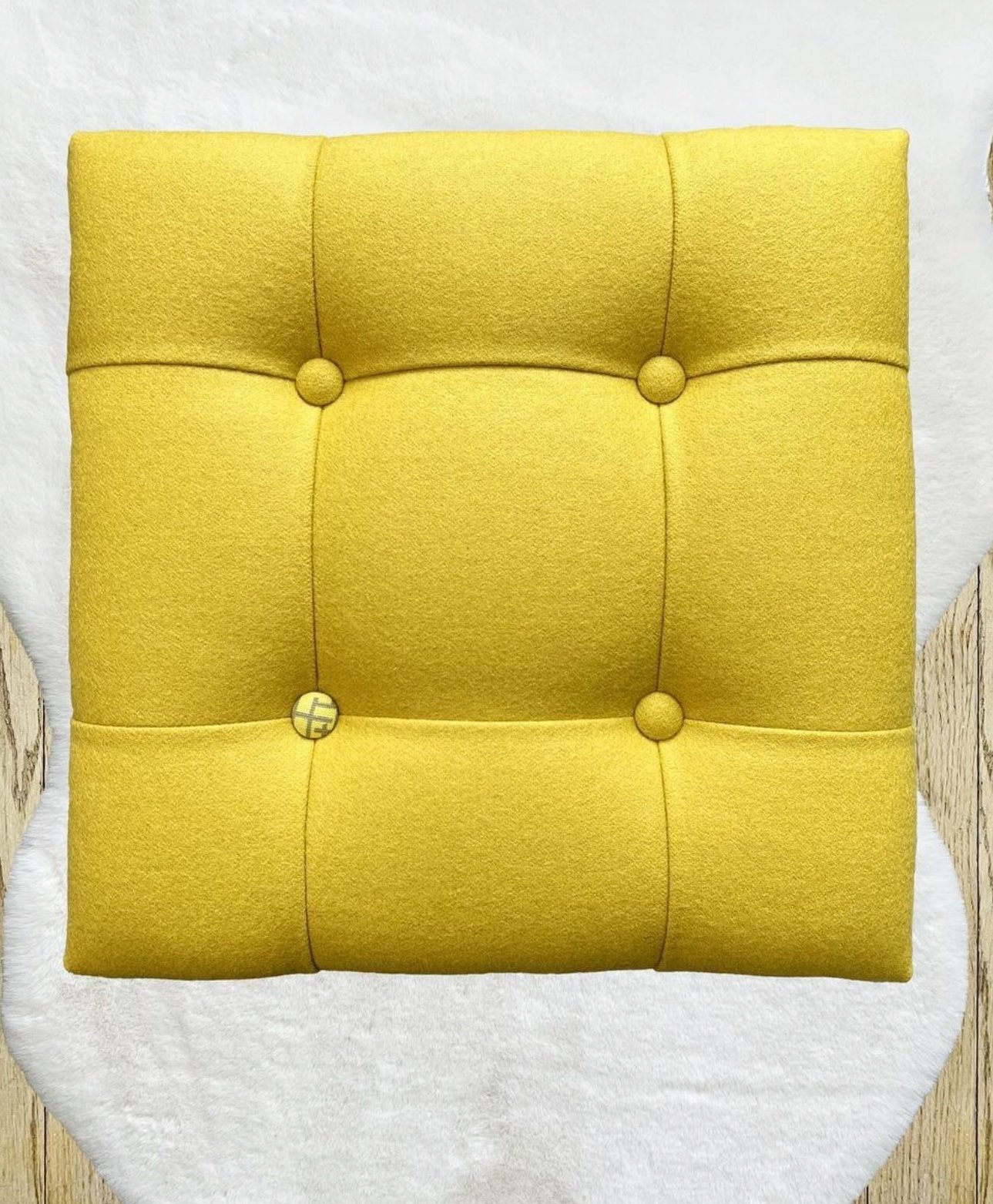 Yellow tufted upholstered armchair with button details, placed on a white fur rug on a wooden floor.