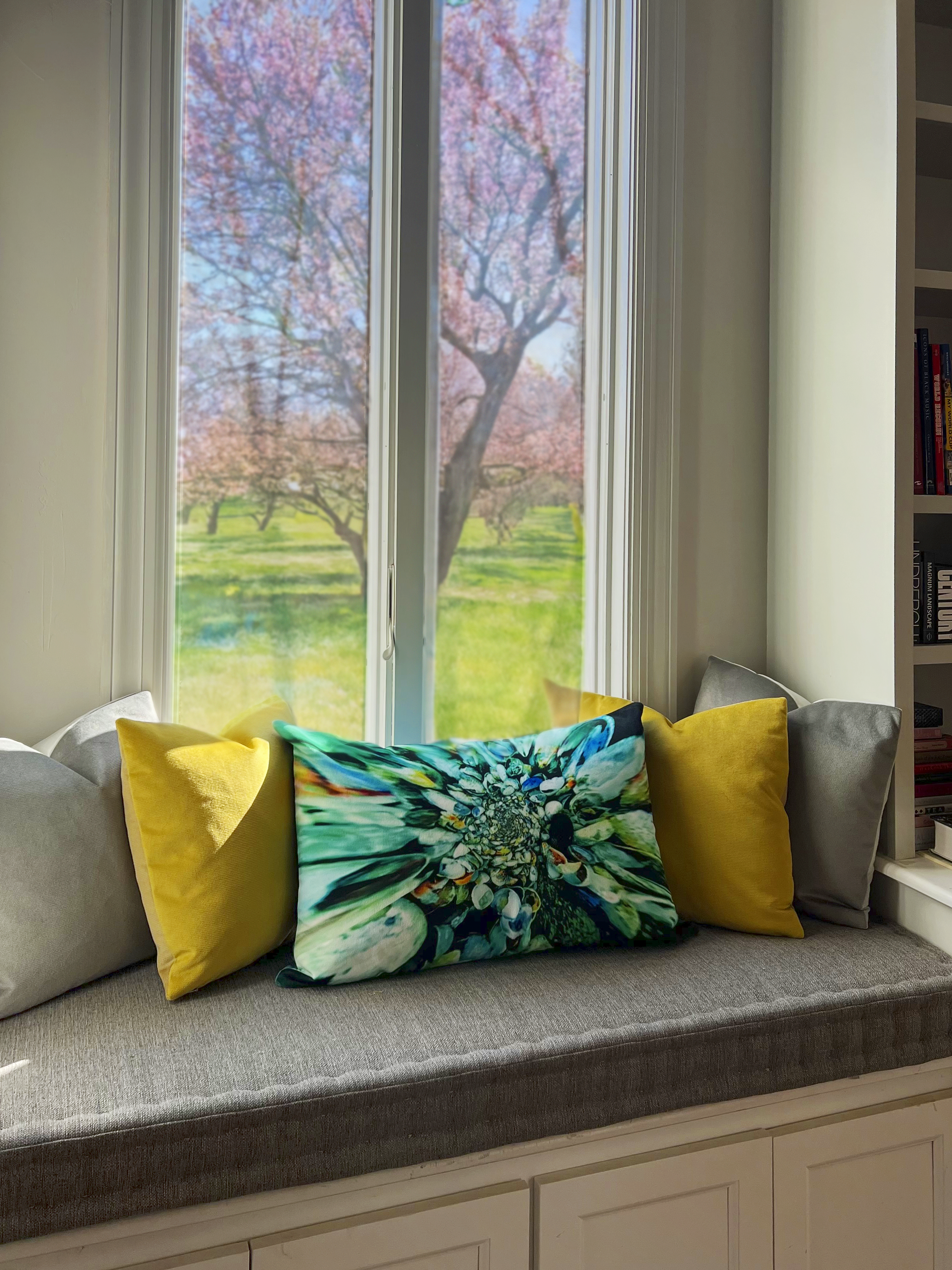 A windowsill with colorful custom throw pillows and a custom cushion for the bench, with a view of pink blossoming trees outside.