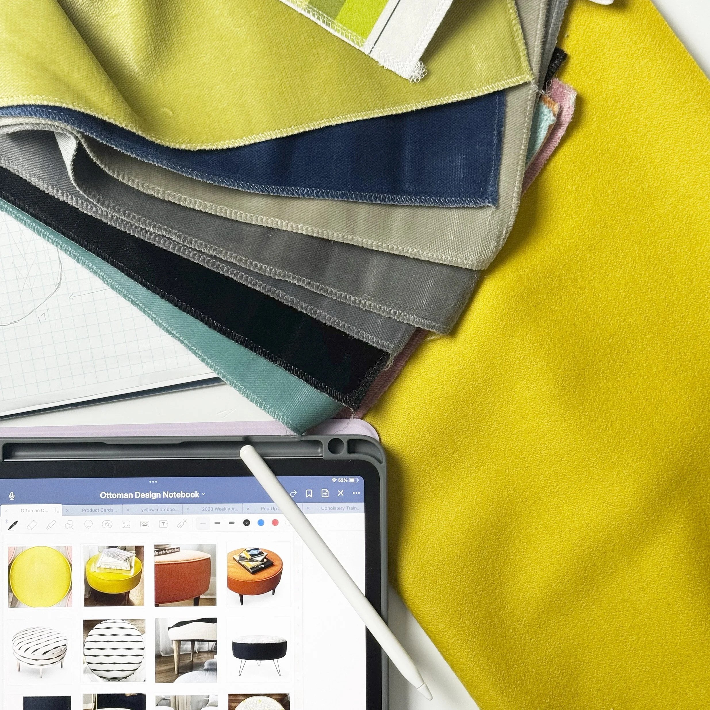A close-up of fabric swatches in various colors and textures, with a tablet displaying furniture images and a stylus on a yellow fabric surface.