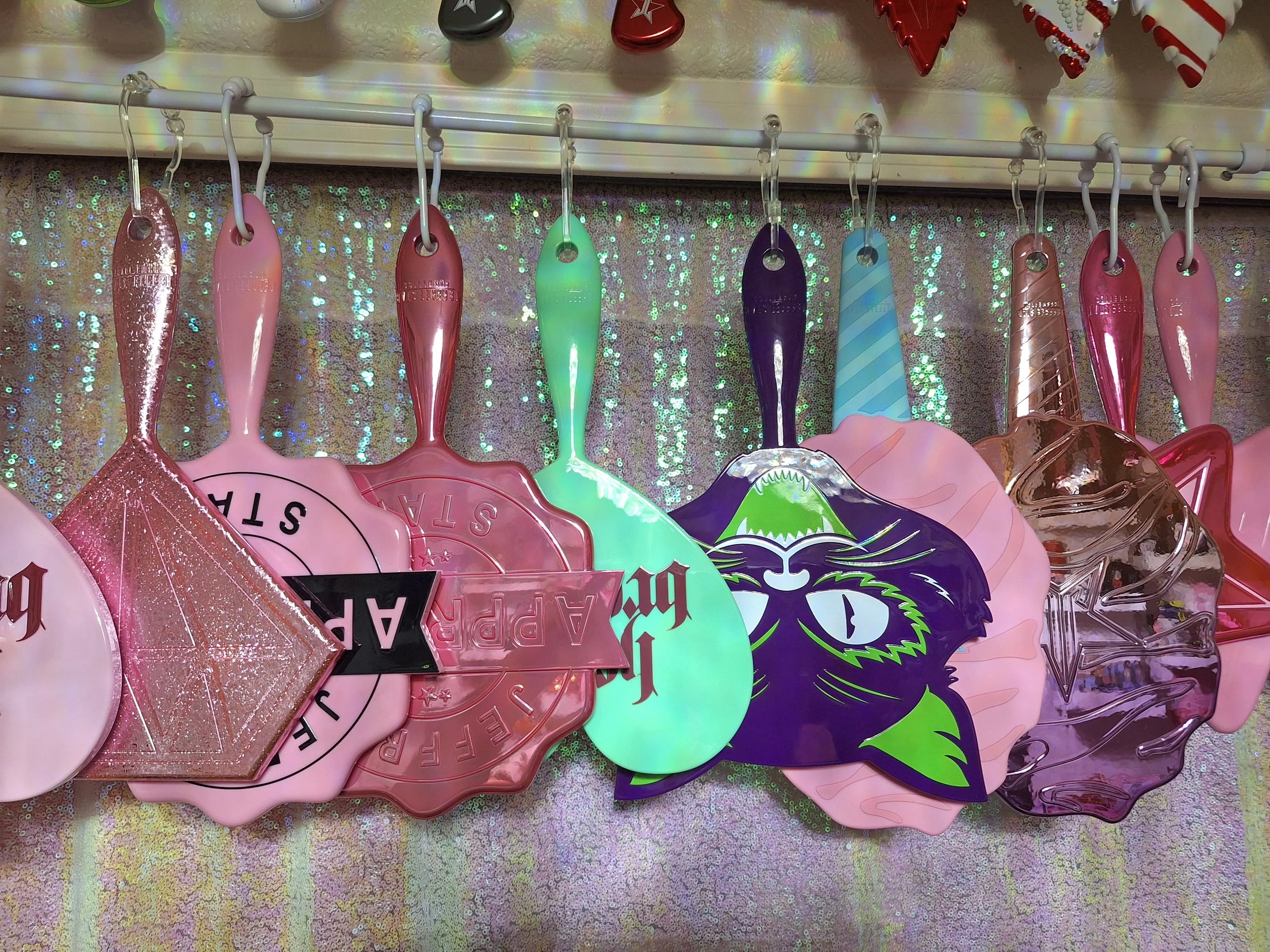 Decorative plastic wall hangings in the shapes of hearts, diamonds, and other shapes with various designs, hanging on hooks against a shimmering, iridescent background.