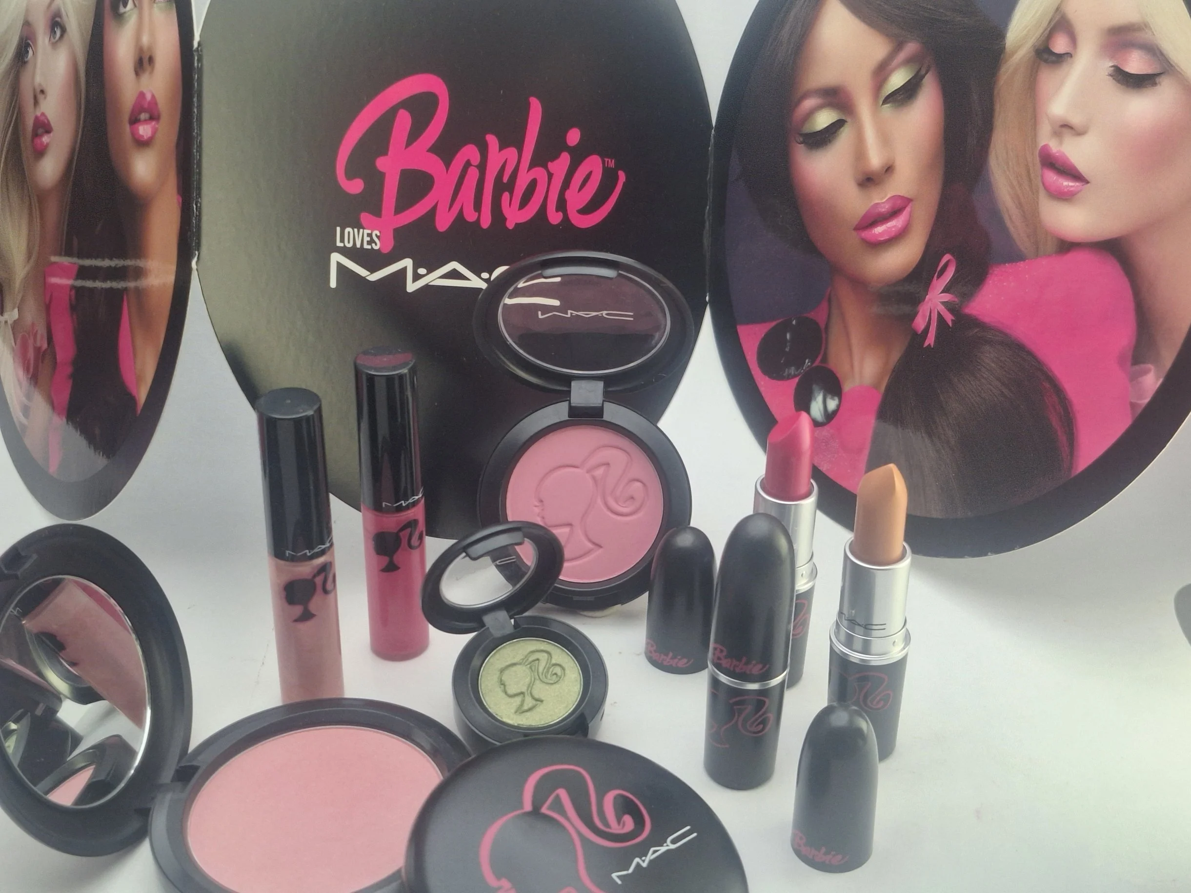 A collection of Barbie-themed makeup products, including blush, lipstick, and eyeshadow, displayed with Barbie imagery and branding.