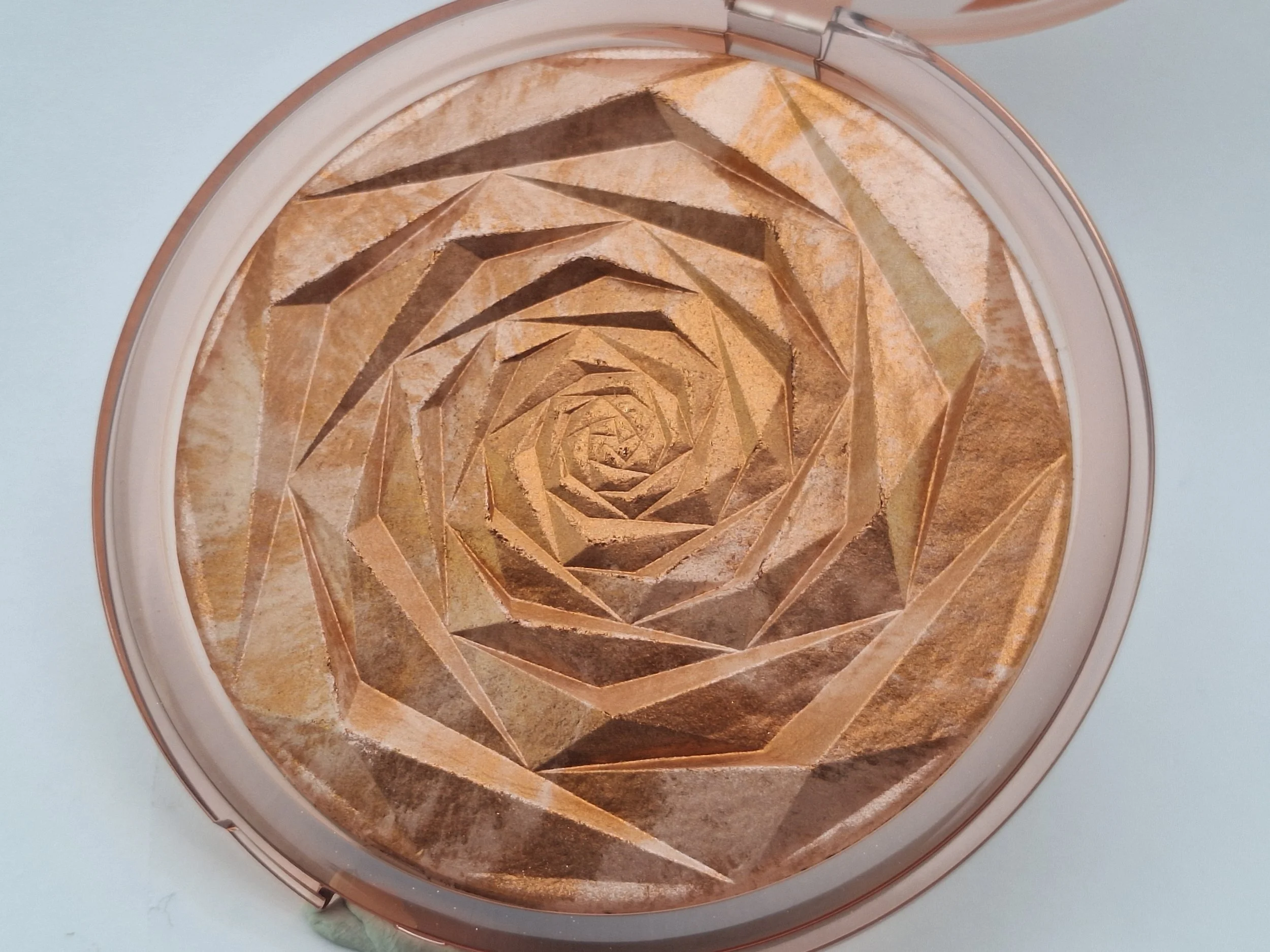 A compact mirror with a geometric spiral pattern inside, featuring shades of gold, bronze, and brown.
