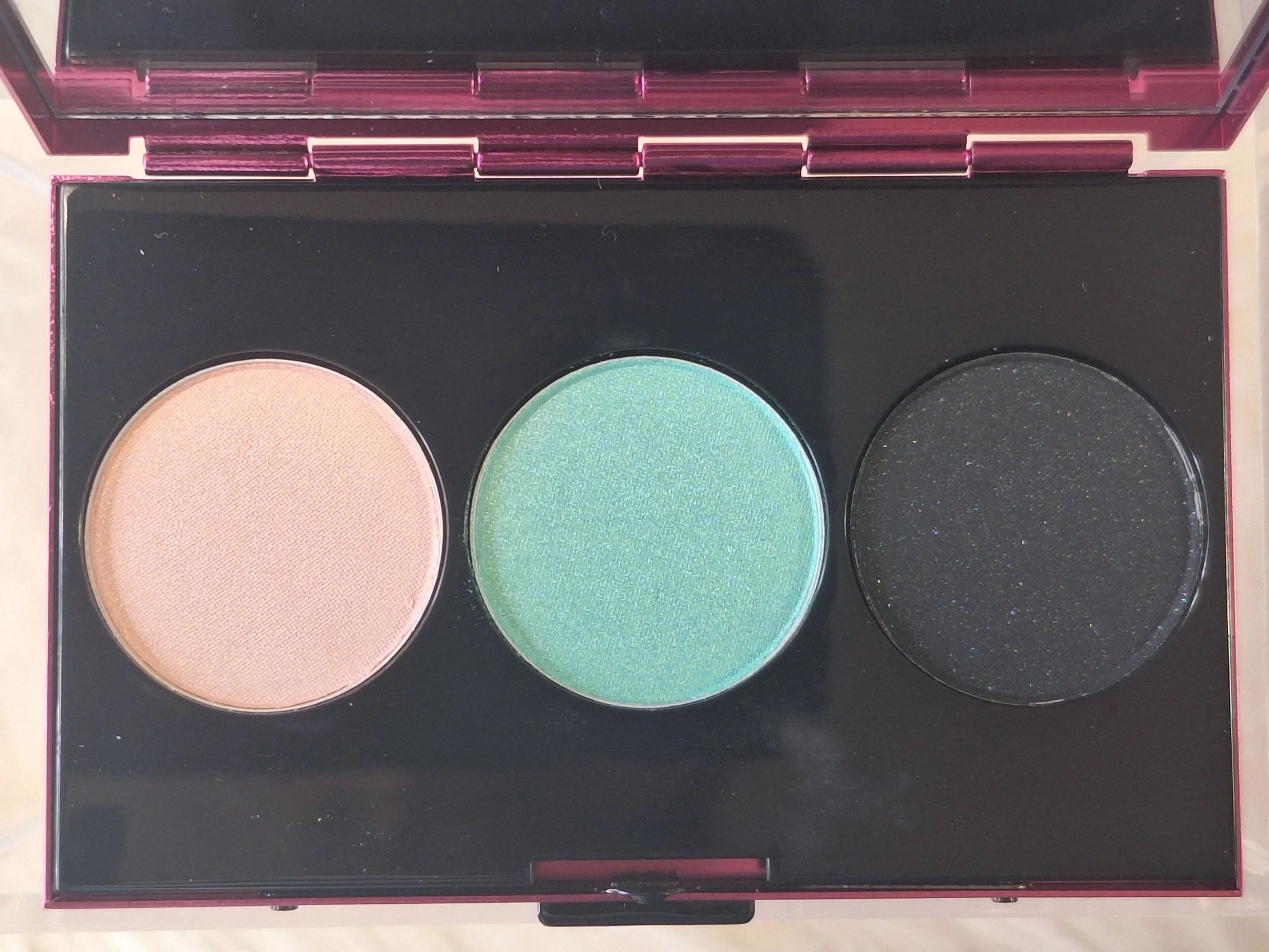 Open Heatherette eyeshadow trio with three vibrant shades—champagne, mint green, and deep black.