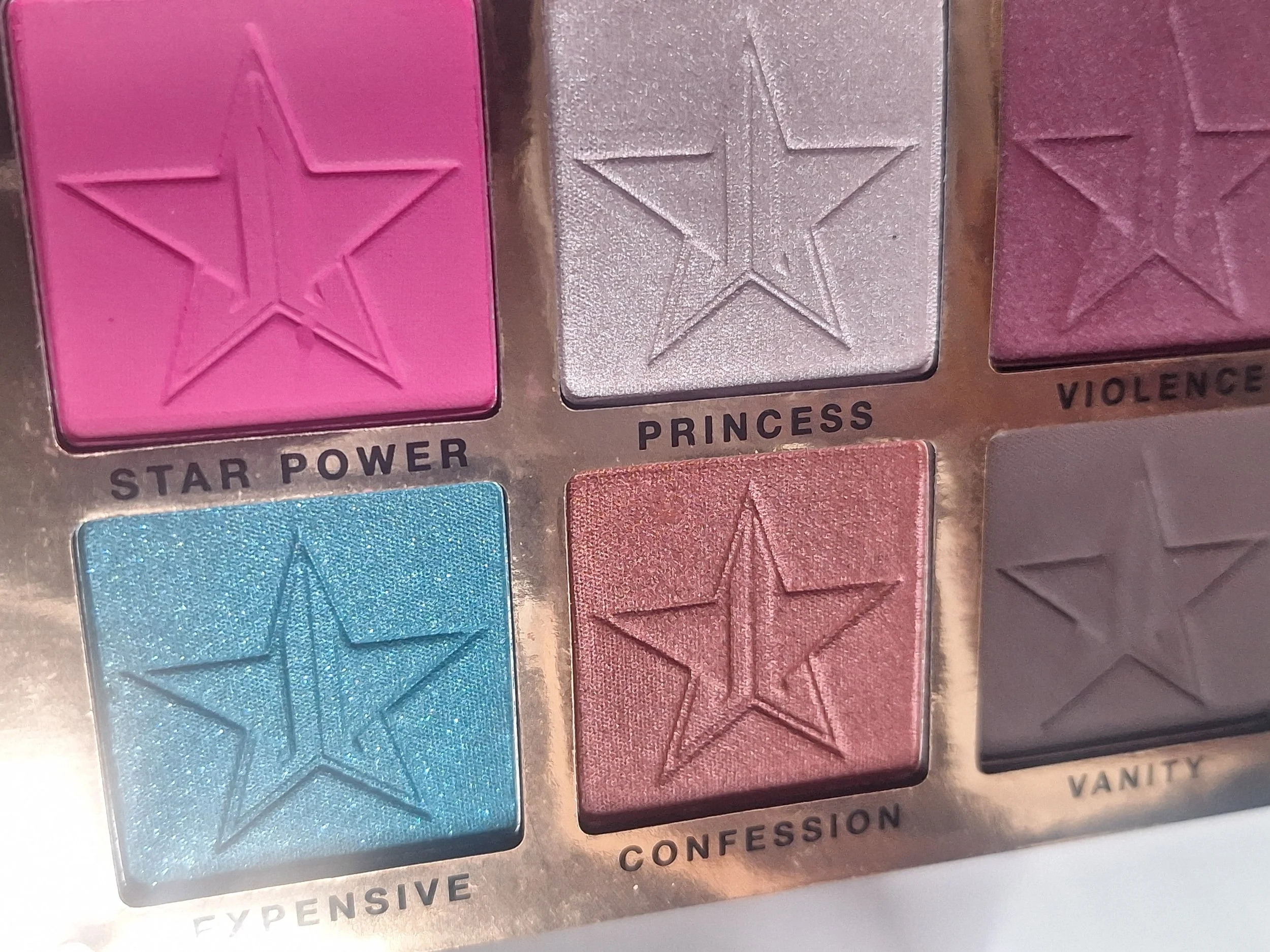 A colorful eyeshadow palette with six shades labeled as Star Power, Princess, Violence, Expensive, Confession, and Vanity, each with a star-shaped embossed pattern.