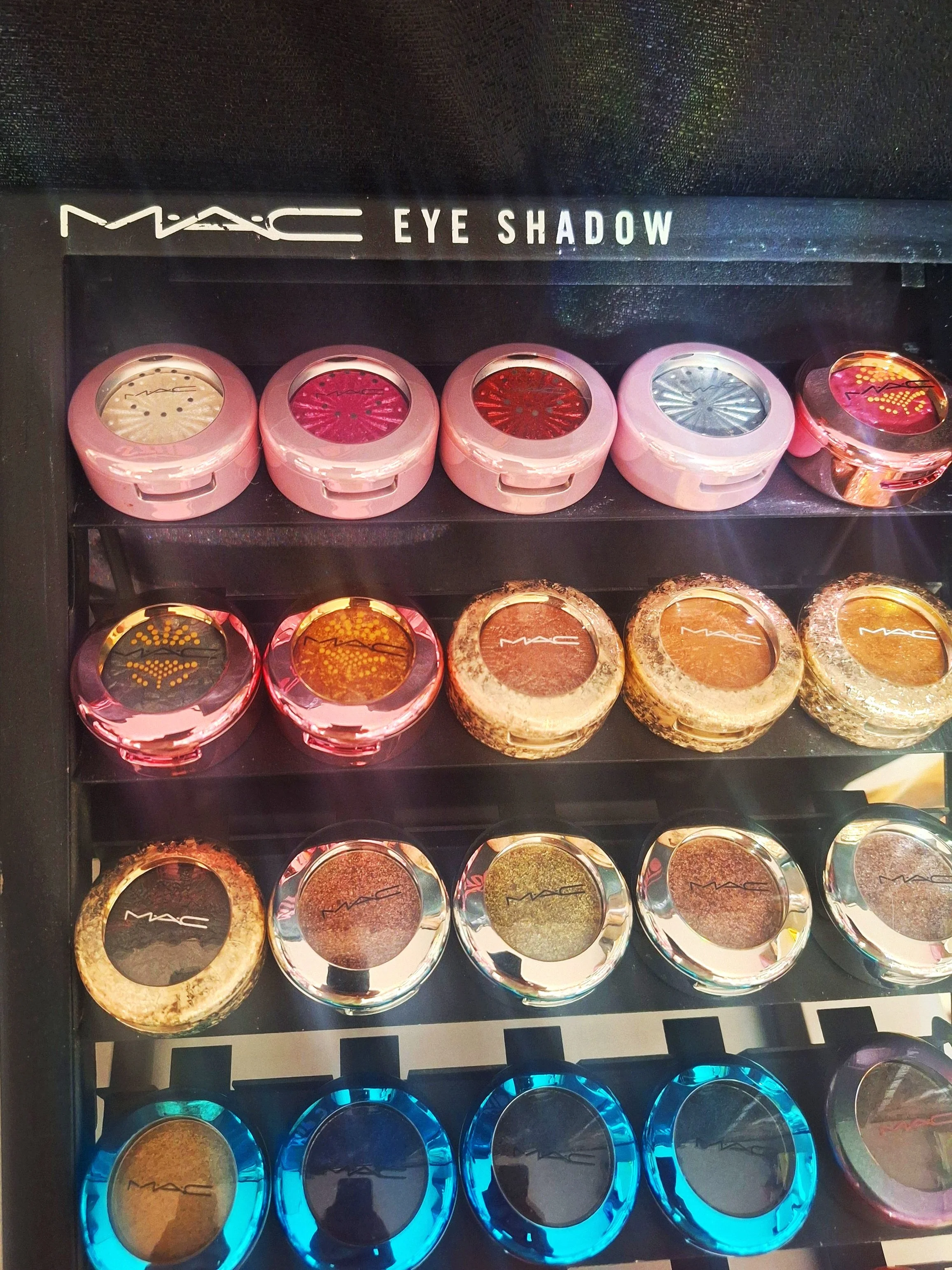 A display case filled with various MAC eyeshadows in round containers arranged in rows with colorful packaging.