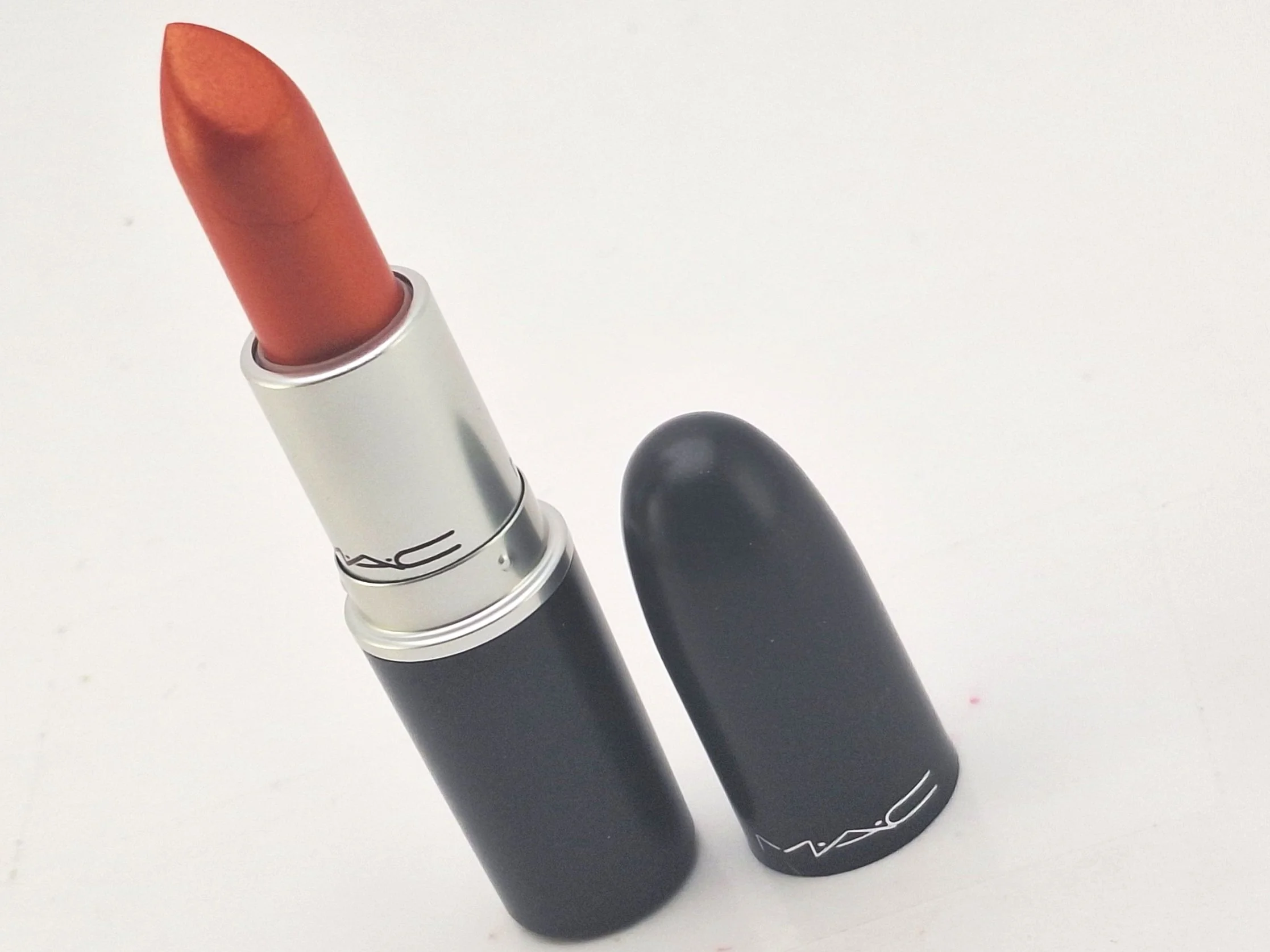 A tube of MAC lipstick, with the cap removed, revealing the lipstick in a peachy shade, placed on a white surface.