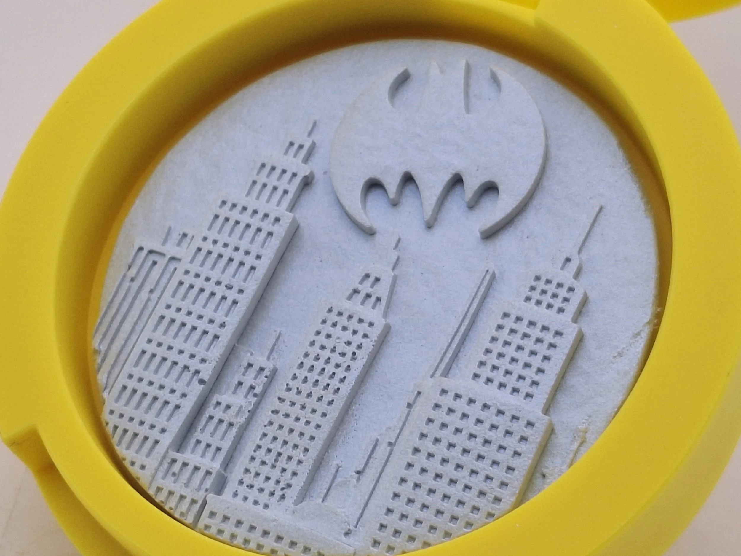 Miniature replica of buildings and the Batman logo, placed inside a yellow circular frame.