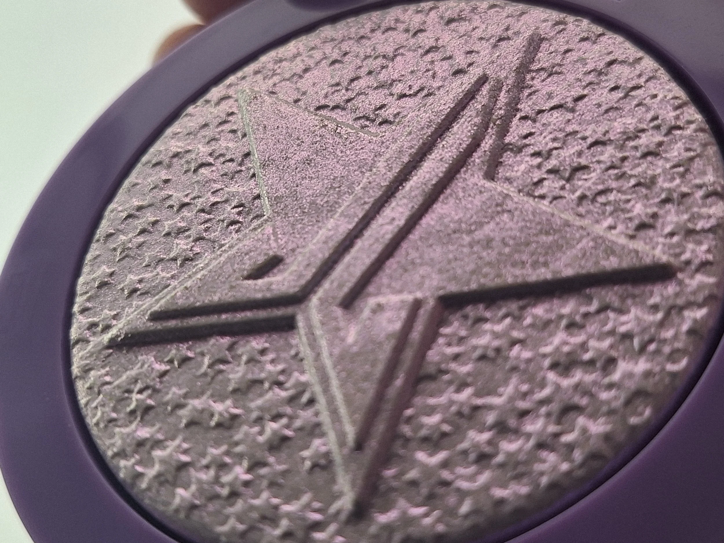 Close-up of a purple, textured eyeshadow compact with the Jeffree Star logo engraved on the surface.