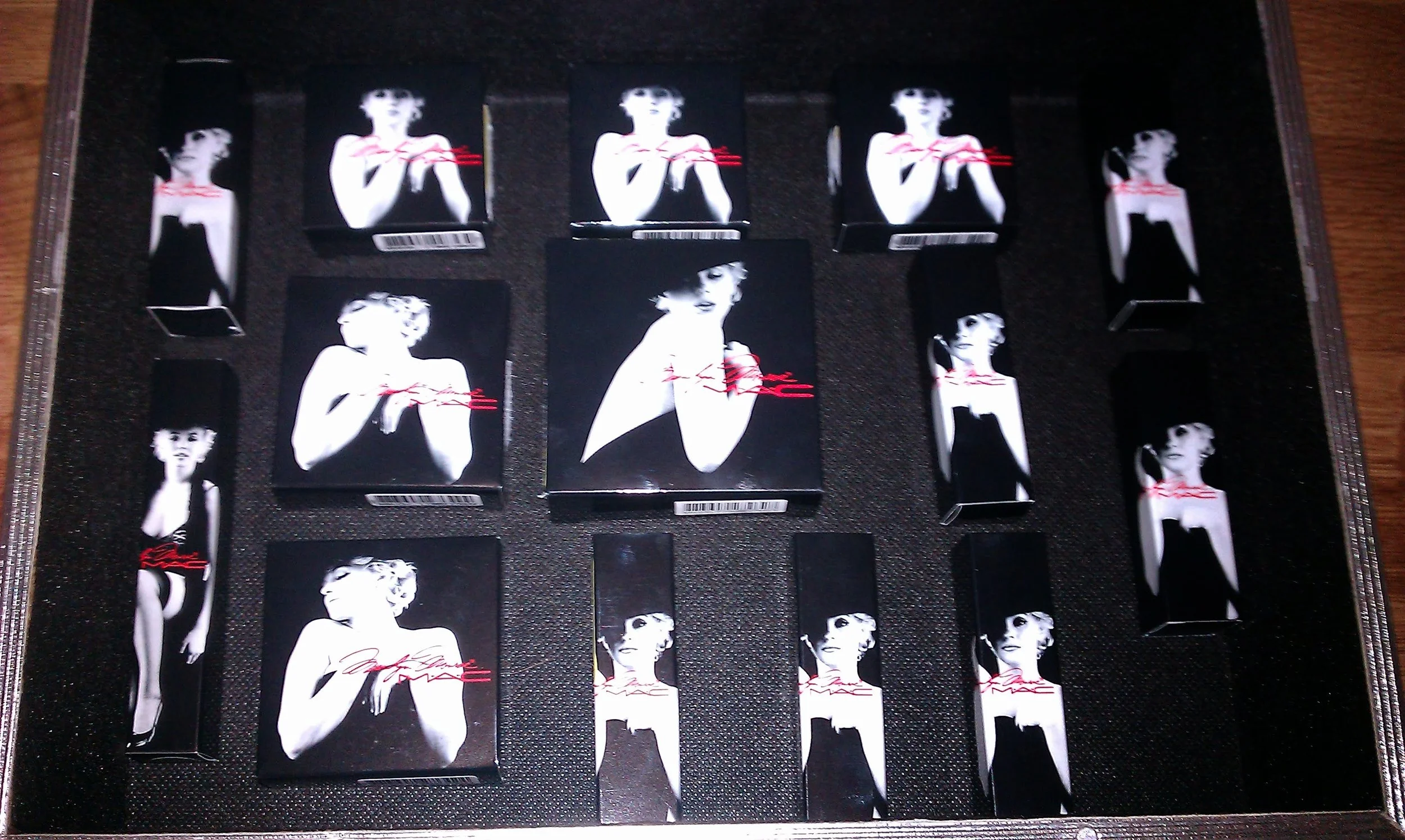 Collection of small black packaging boxes with a black and white image of a woman's face and red text on a black background, arranged on a black foam tray.