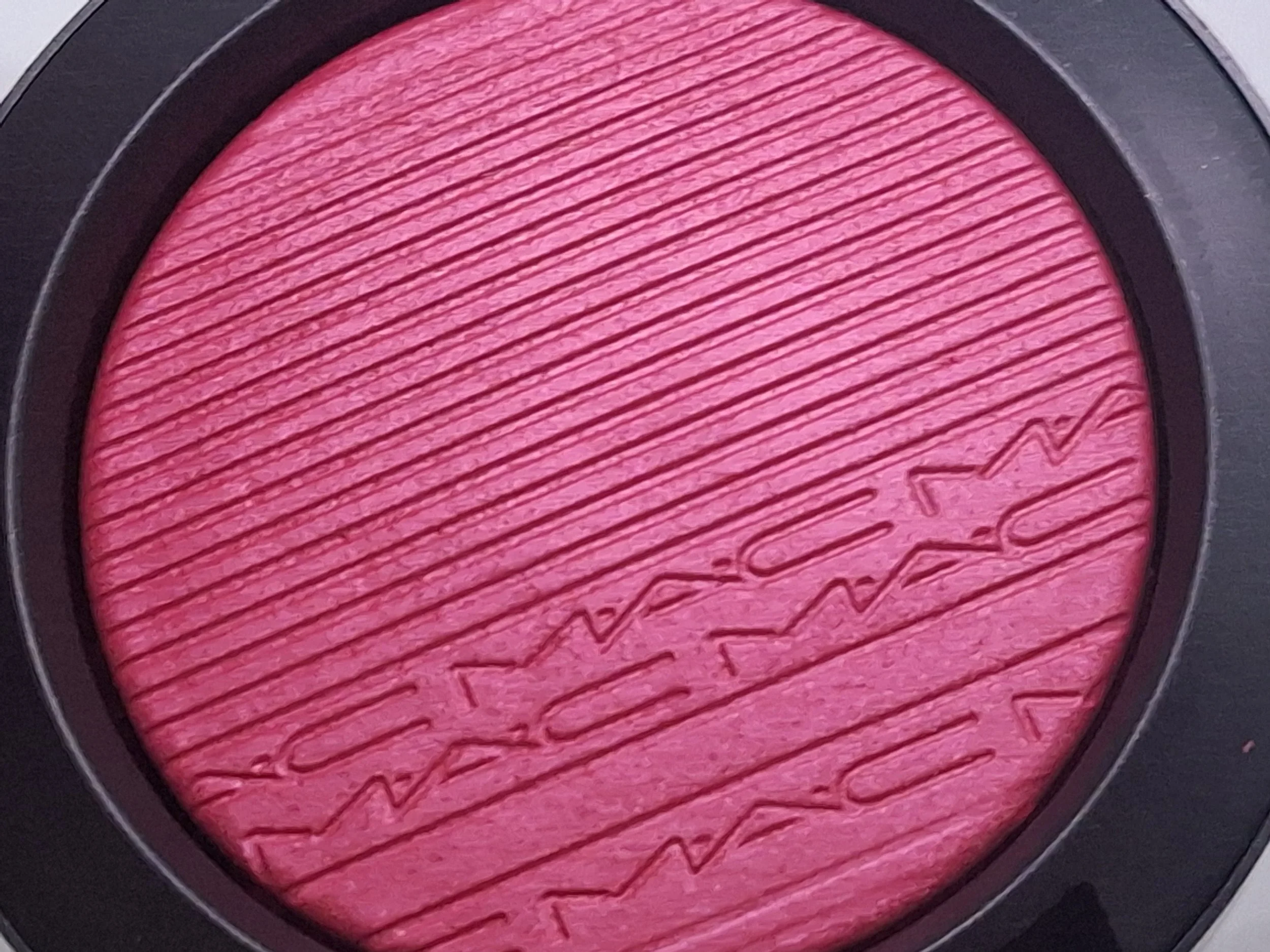 Close-up of a pink MAC blush with textured surface and the brand name lightly engraved into the product.