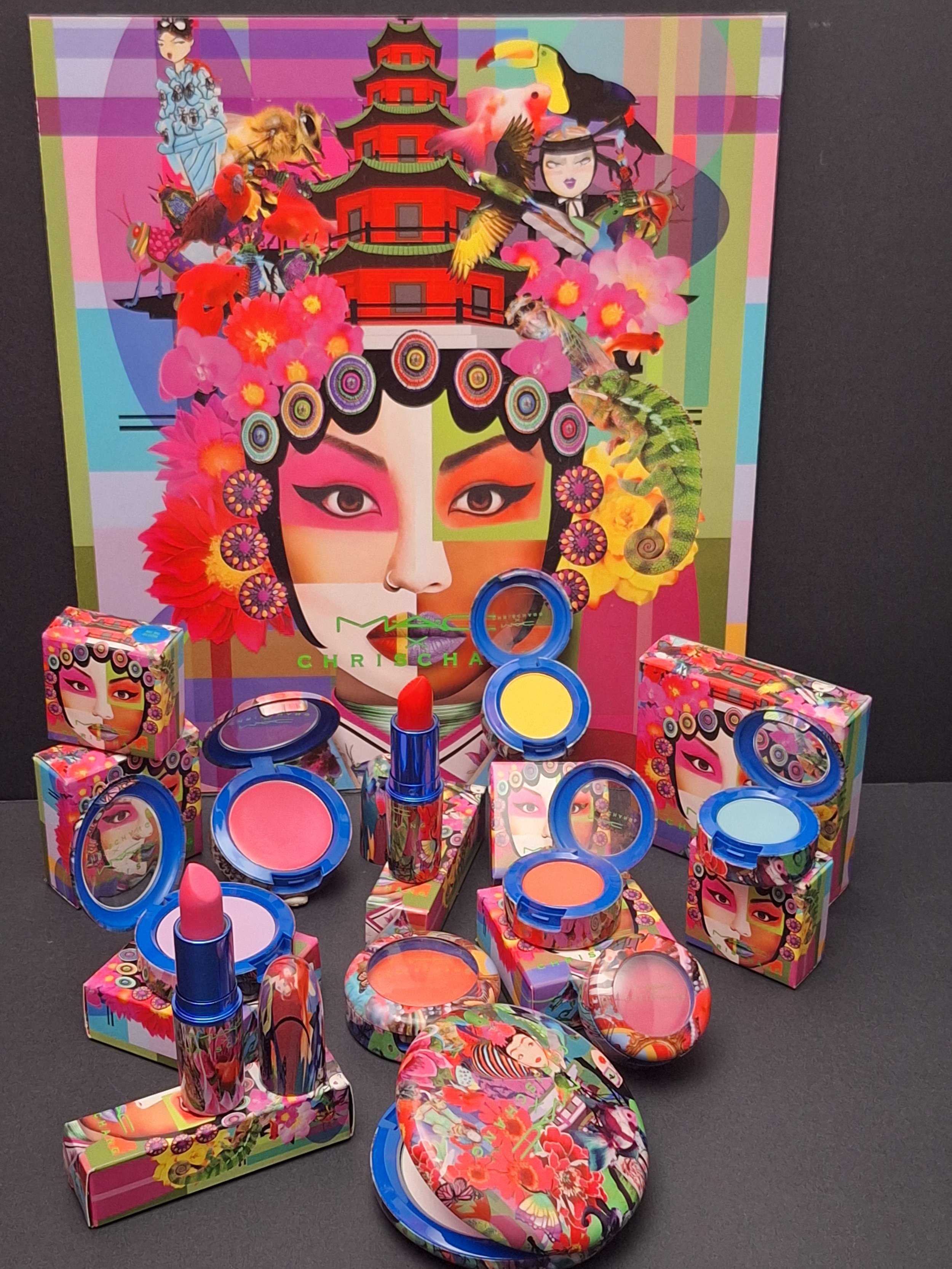 Colorful collection of makeup products and boxes featuring a vibrant, artistic design with a woman's face, surrounded by flowers, animals, and cultural elements, with packaging and product containers matching the vivid artistic theme.