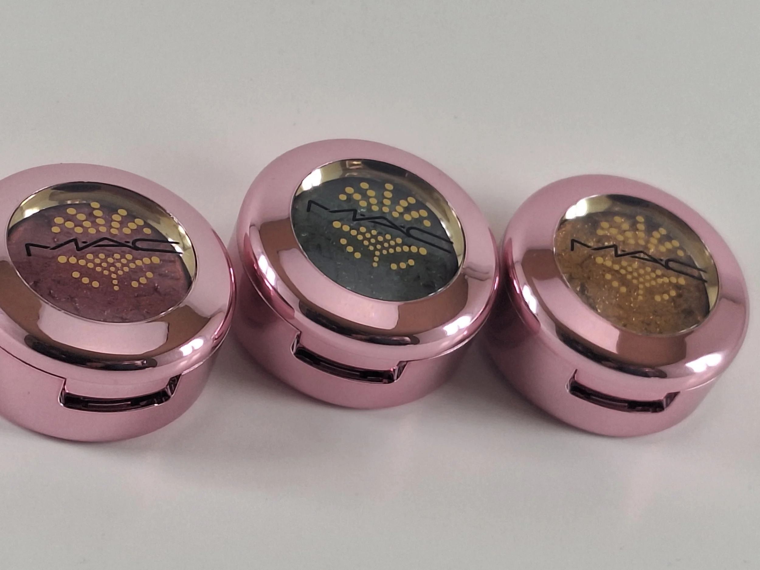 Three pink MAC cosmetic containers with black and gold patterned tops on a white surface.