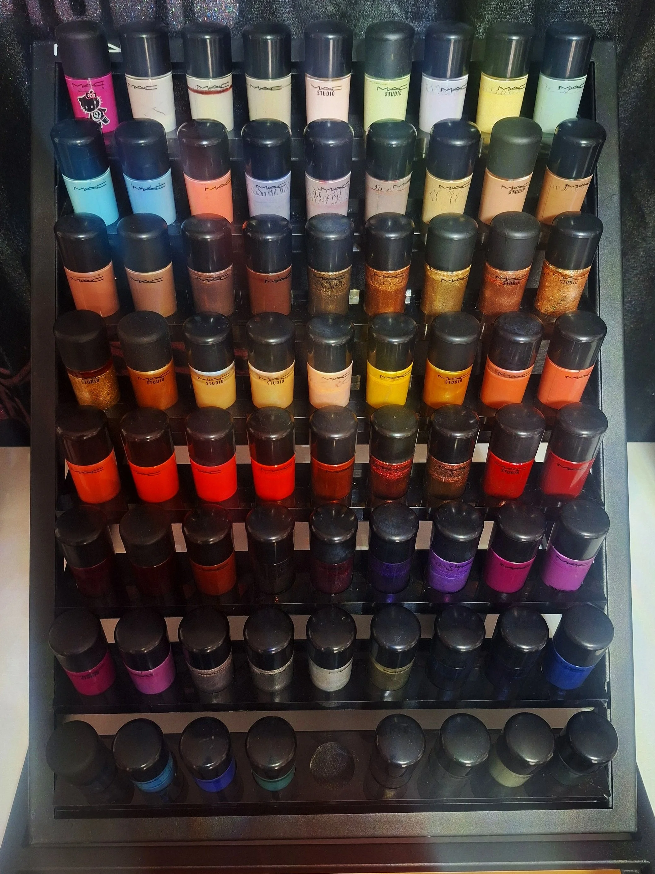 A display of various MAC makeup foundation bottles arranged on a black tiered rack.