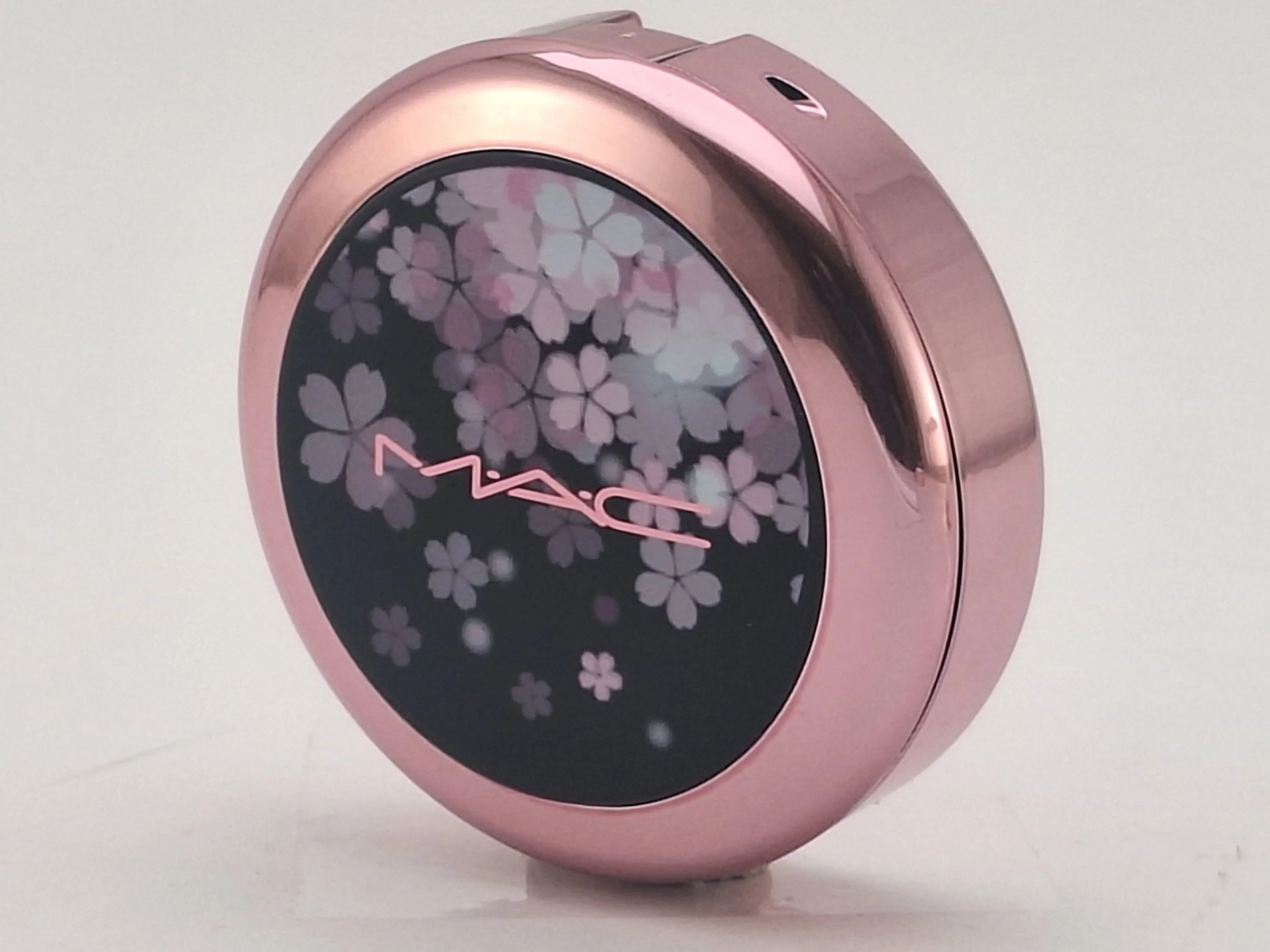 A round MAC computer mouse with a pink metallic finish and a floral display on its screen.