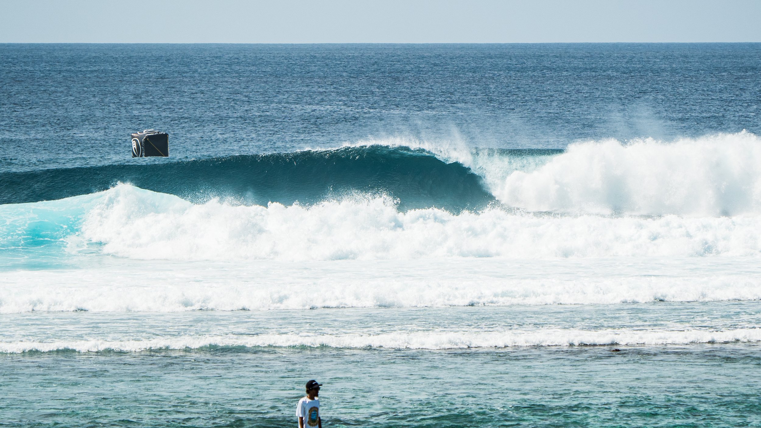 Ocean wave breaking, with a surfer in the foreground.