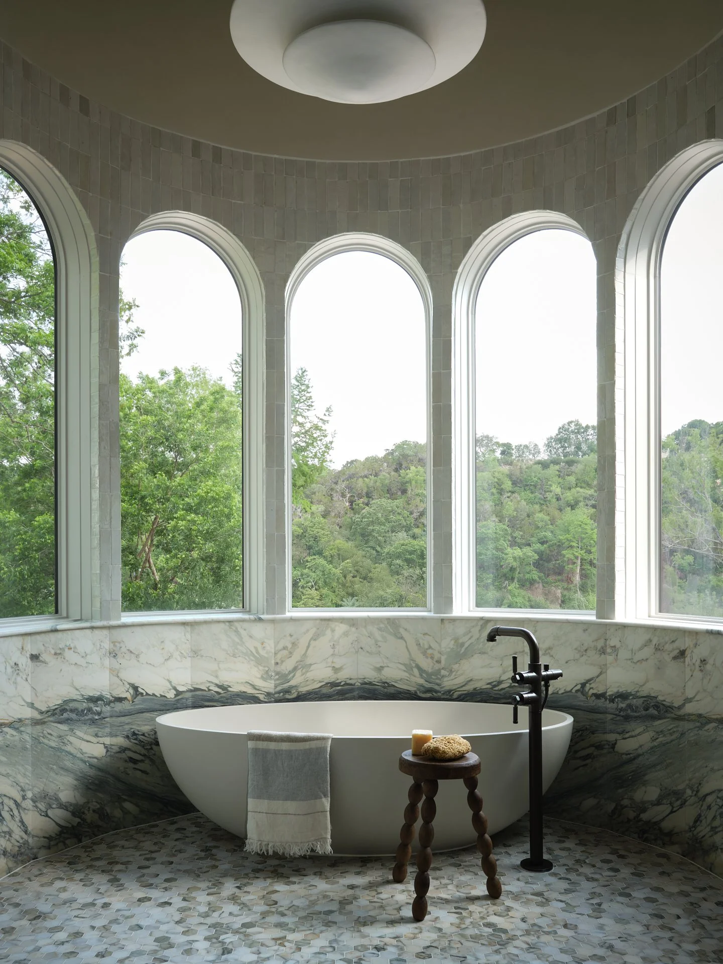 large bathtub surrounded by marble and arched windows surrounding the room.