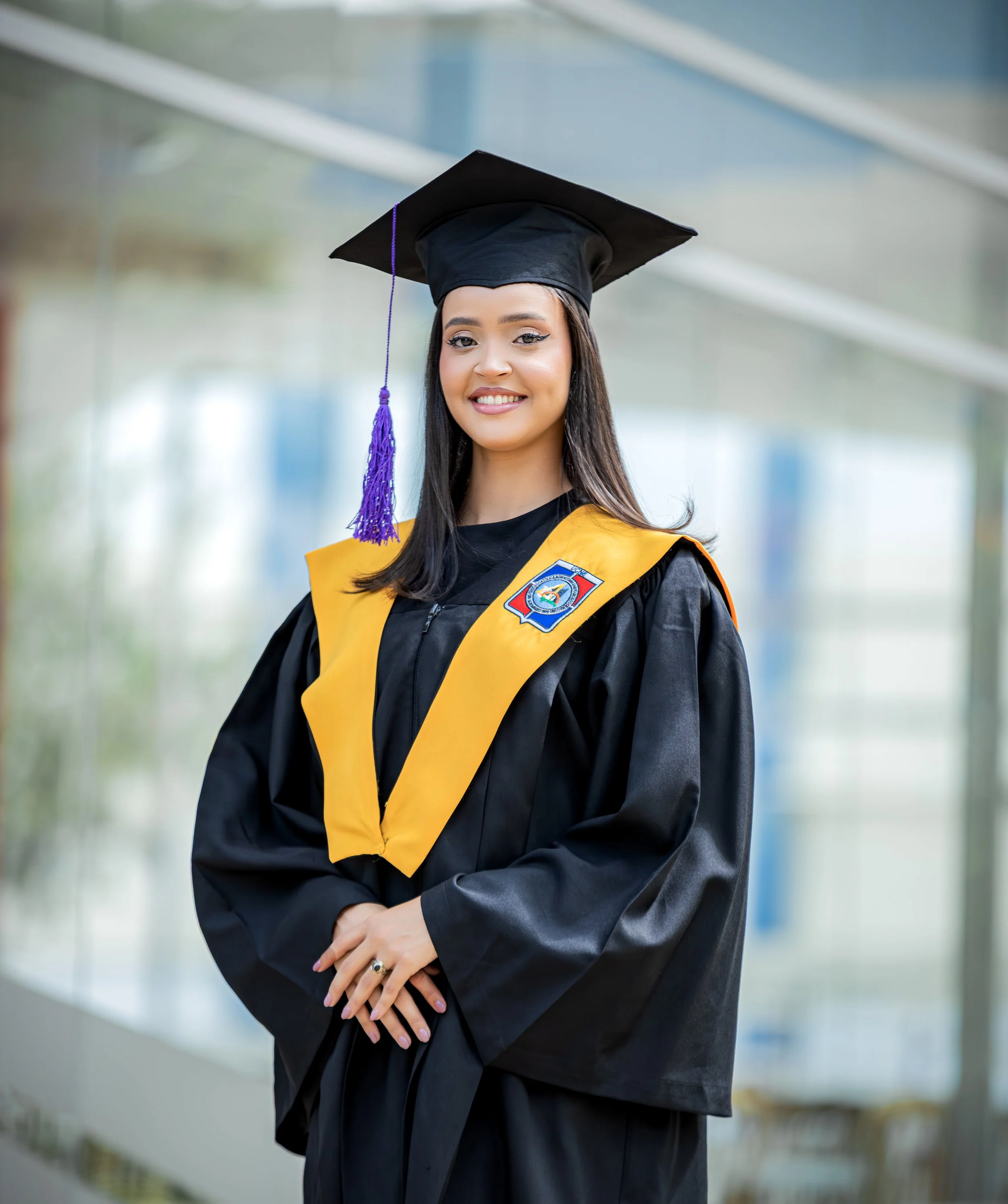 Joven mujer con toga y sombrero de graduación en un entorno moderno, sonriendo y mostrando su acto de graduación.