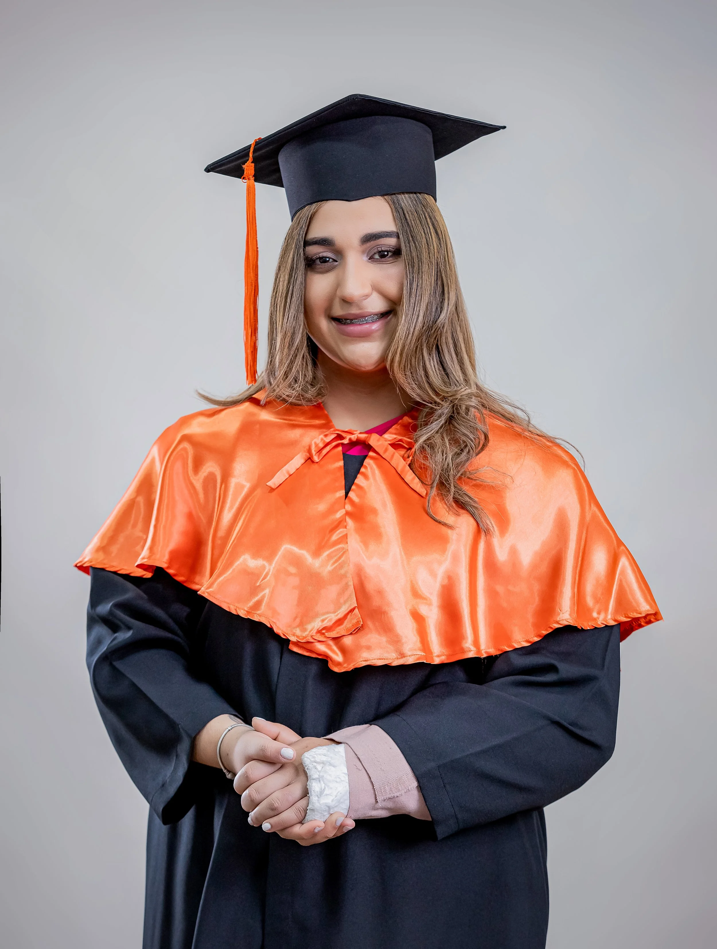 Joven mujer con toga y birrete de graduación sosteniendo las manos juntas frente a ella