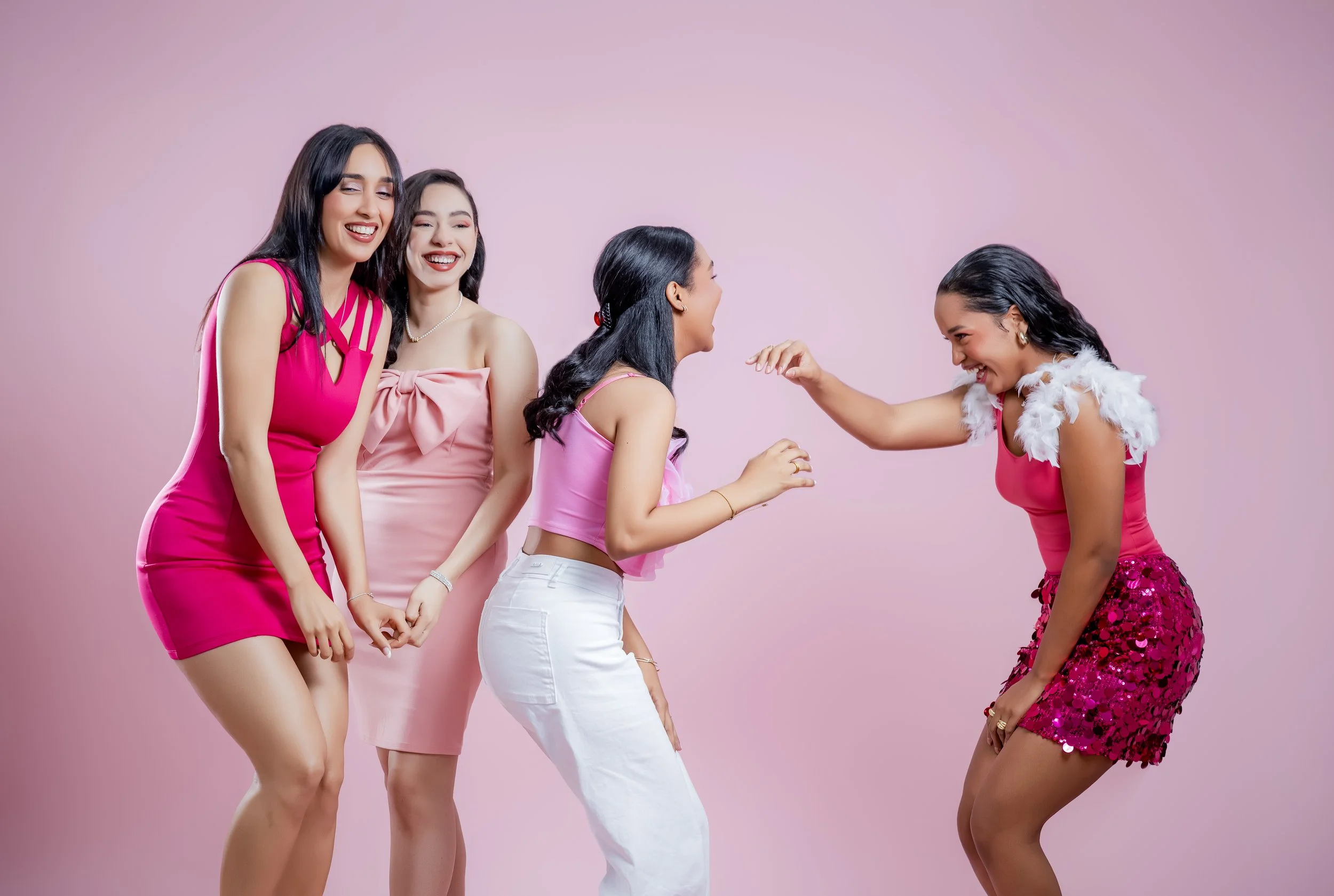 Cuatro mujeres jóvenes festejando y riendo juntas en un fondo rosa