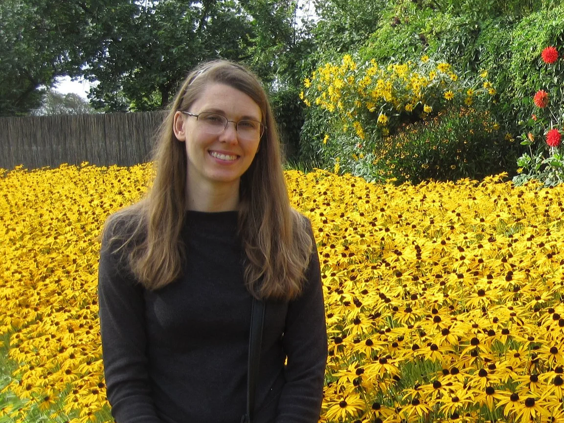 Counselor Heather in a field of yellow flowers wearing a dark grey long-sleeved shirt and glasses