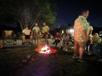 Group of people gathered around a fire pit at night in a backyard