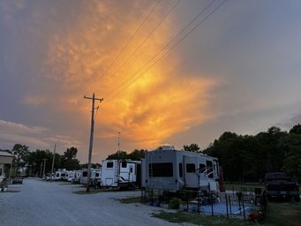 RVs parked in a campground at sunset with dramatic orange and yellow clouds in the sky.