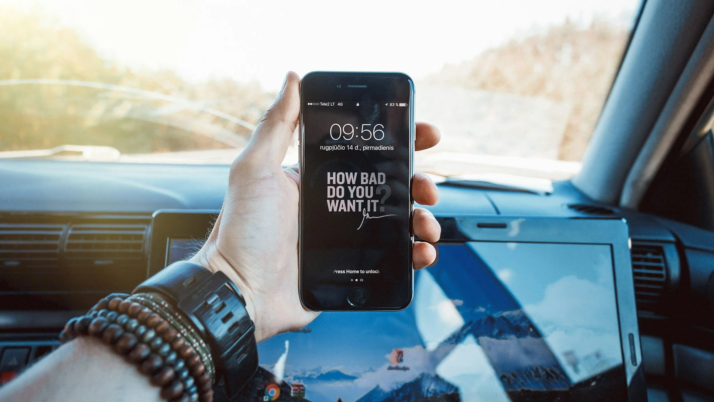 Person inside a vehicle holding a smartphone with a lock screen message that reads 'HOW BAD DO YOU WANT IT?'