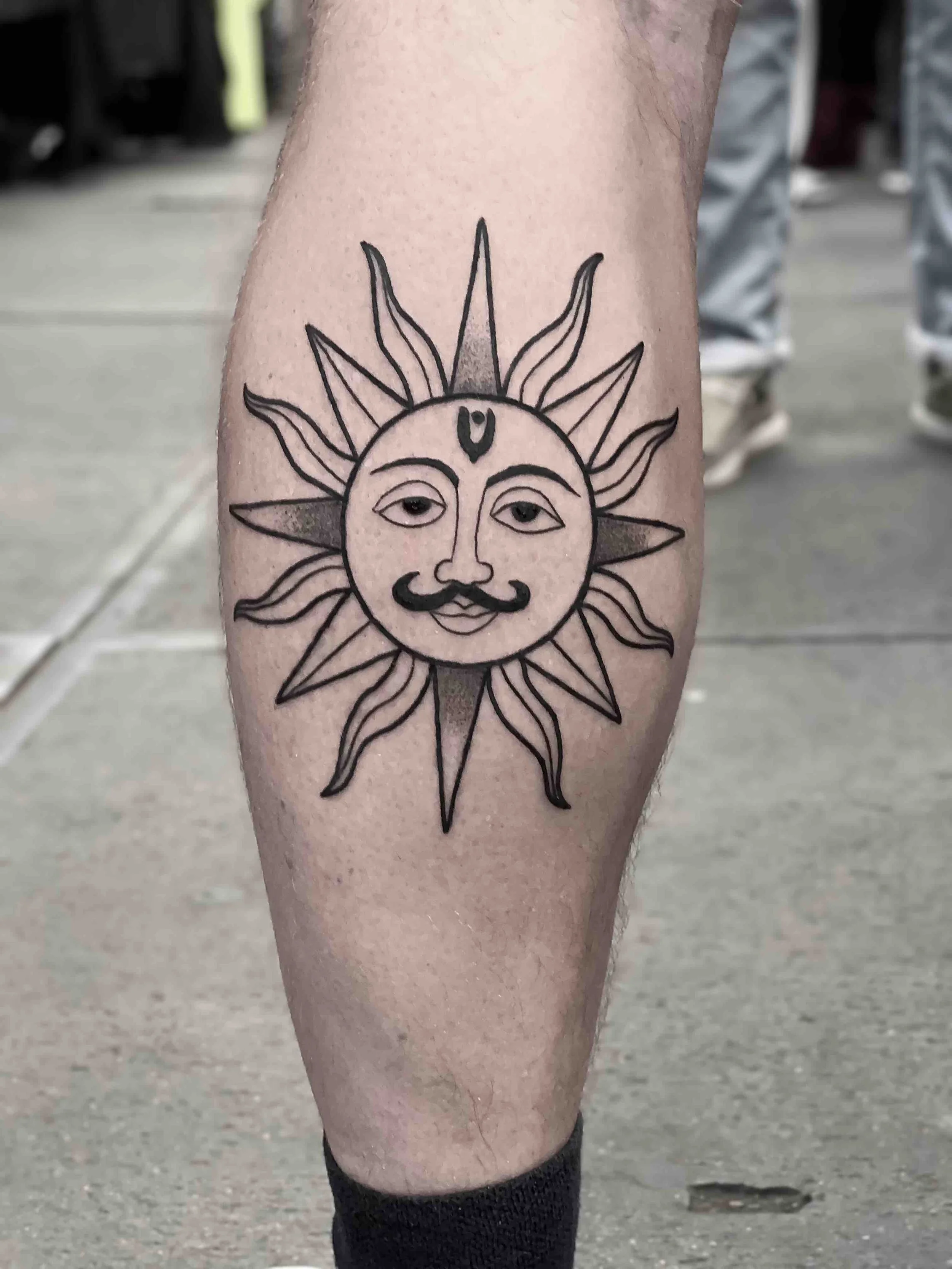Old school zon tattoo met gezicht en snor, gezet door tattoo artiest Jenn bij Se7en Sins Tattoo in Koudum. Een klassiek en speels ontwerp op de kuit — vintage stijl bij de beste tattooshop van Friesland, nabij Sneek, Heerenveen 