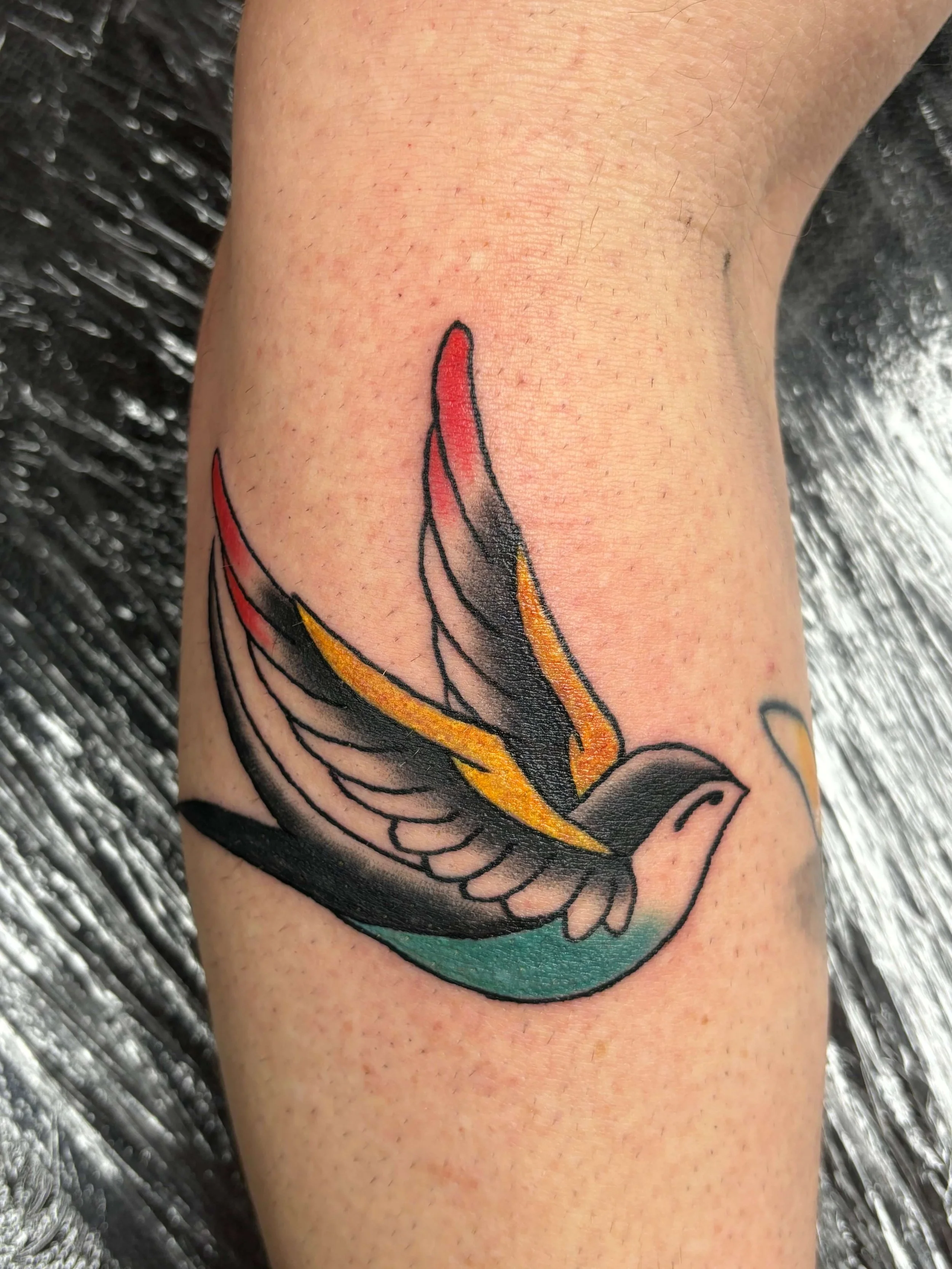 Old school tattoo van een kleurrijke zwaluw, gezet bij Se7en Sins Tattoo in Friesland – klassieke retro tattoo stijl met strakke lijnen en levendige kleuren