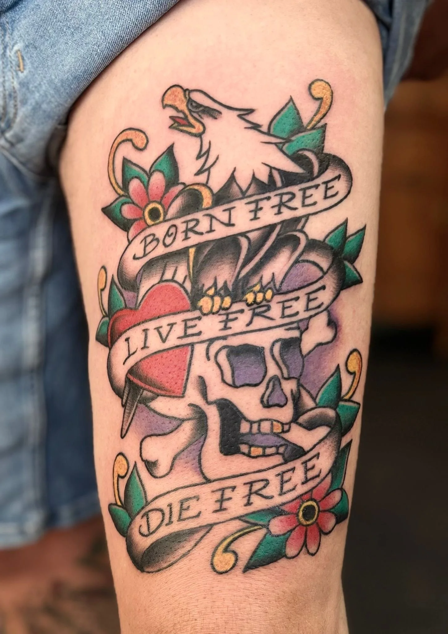 Old school tattoo van een schedel met bloemen en arendkop, inclusief de tekst ‘born free, live free, die free’, gezet door Jurjen Wielenga bij Se7en Sins Tattoo nabij Sneek, Heerenveen, Lemmer en Leeuwarden.
