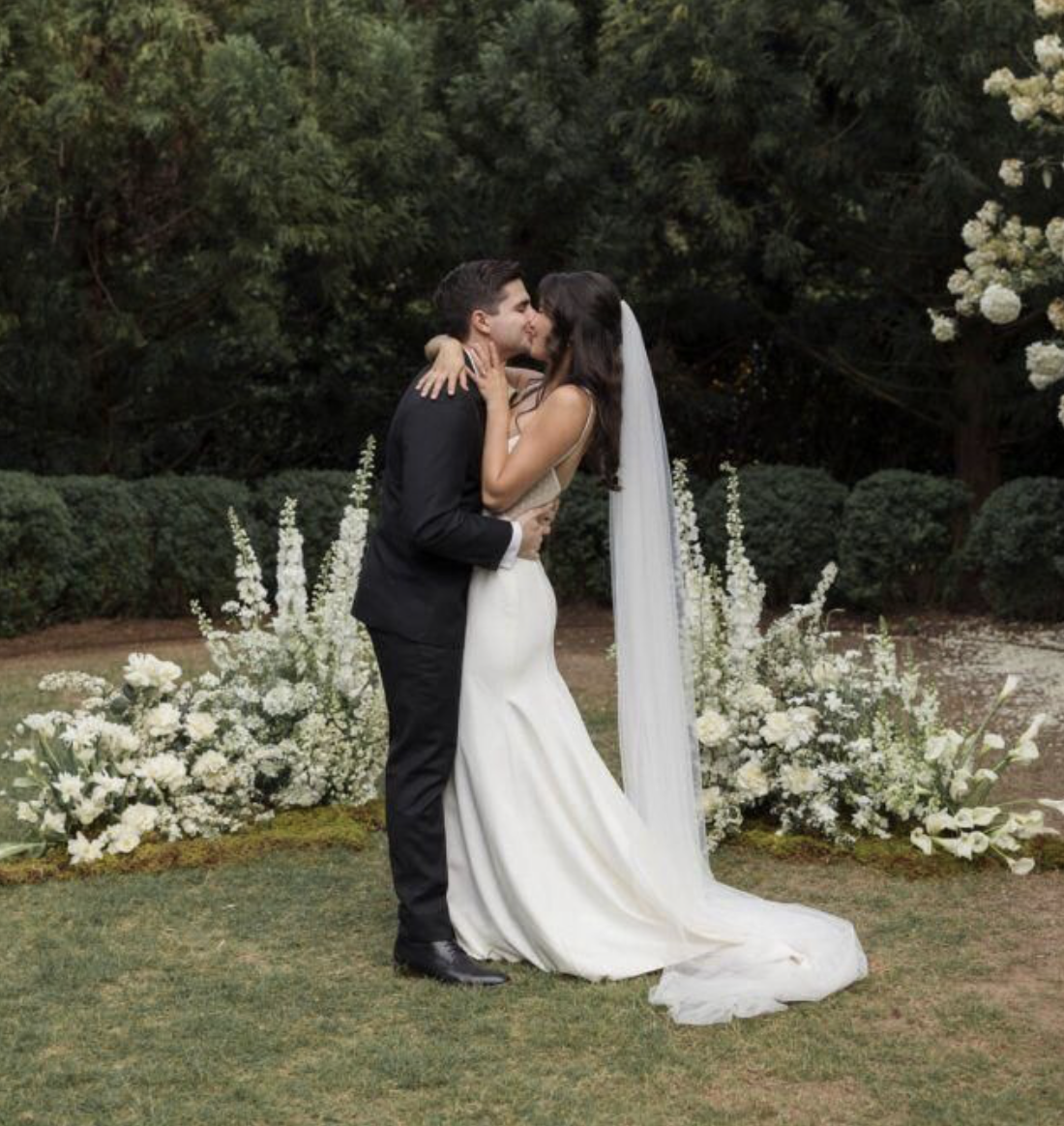 Couple Kissing At Wedding with Flowers Behind Them