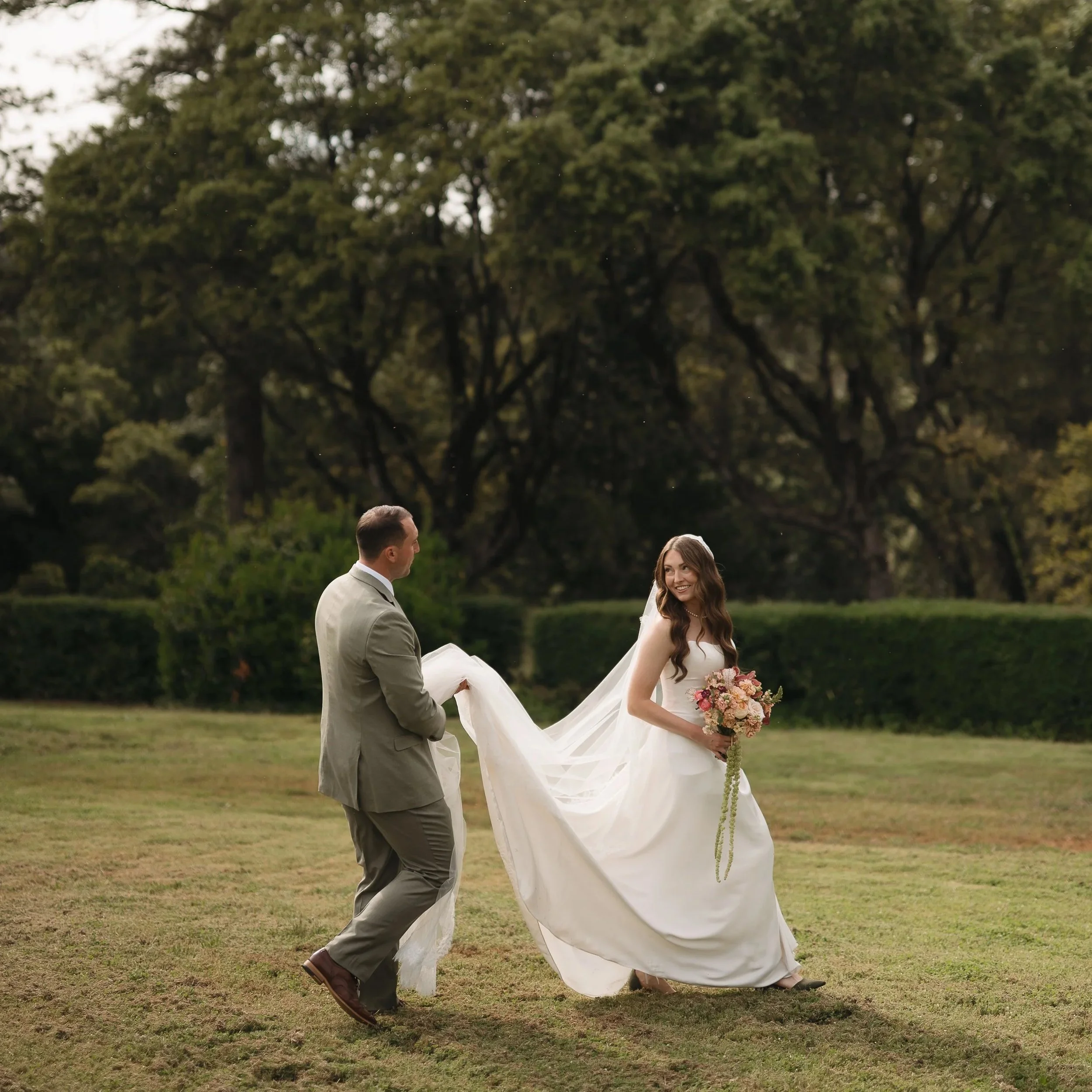 Couple getting married. Bride holding bouquet by Golden Flowers. Groom holding bride's dress