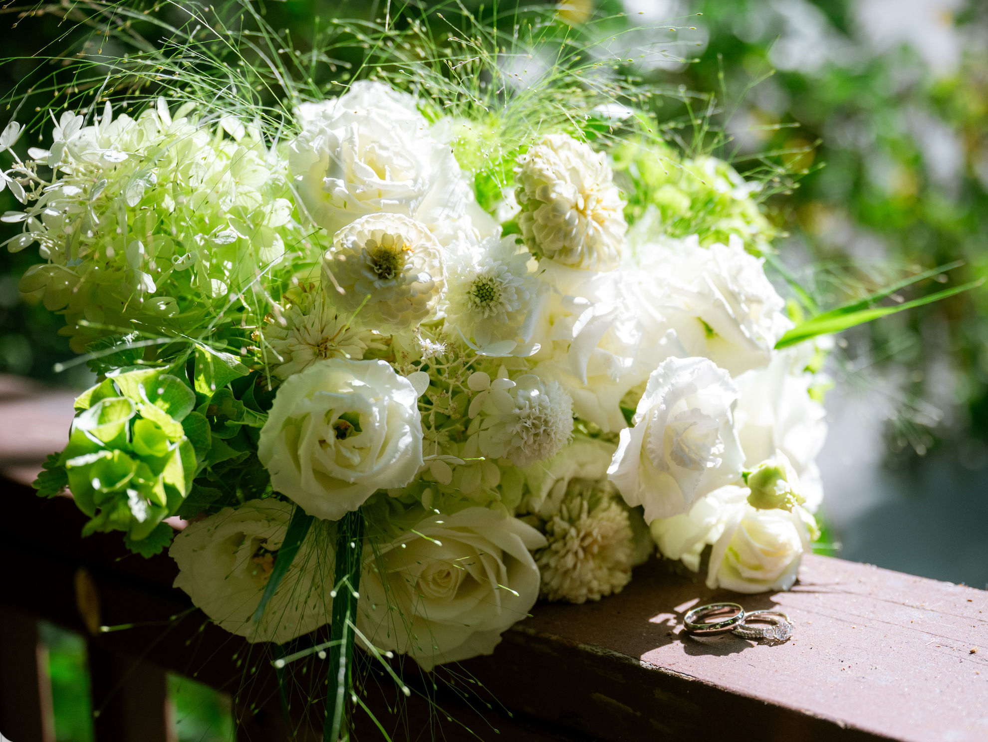 A wedding bouquet with white flowers and two wedding rings resting on a wooden surface. Wedding was at the stonehouse in Nevada City 