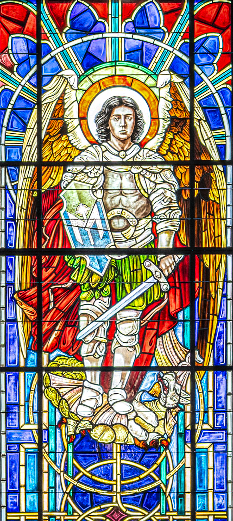 Colorful stained glass window depicting a knight with wings, holding a sword and shield, standing on a dragon, with a halo around his head.