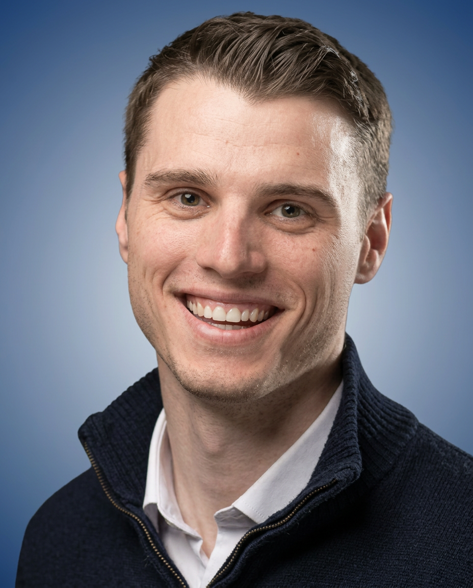 "Smiling man  with short brown hair, wearing a white collared shirt under a dark zip-up sweater, against a smooth blue gradient background.