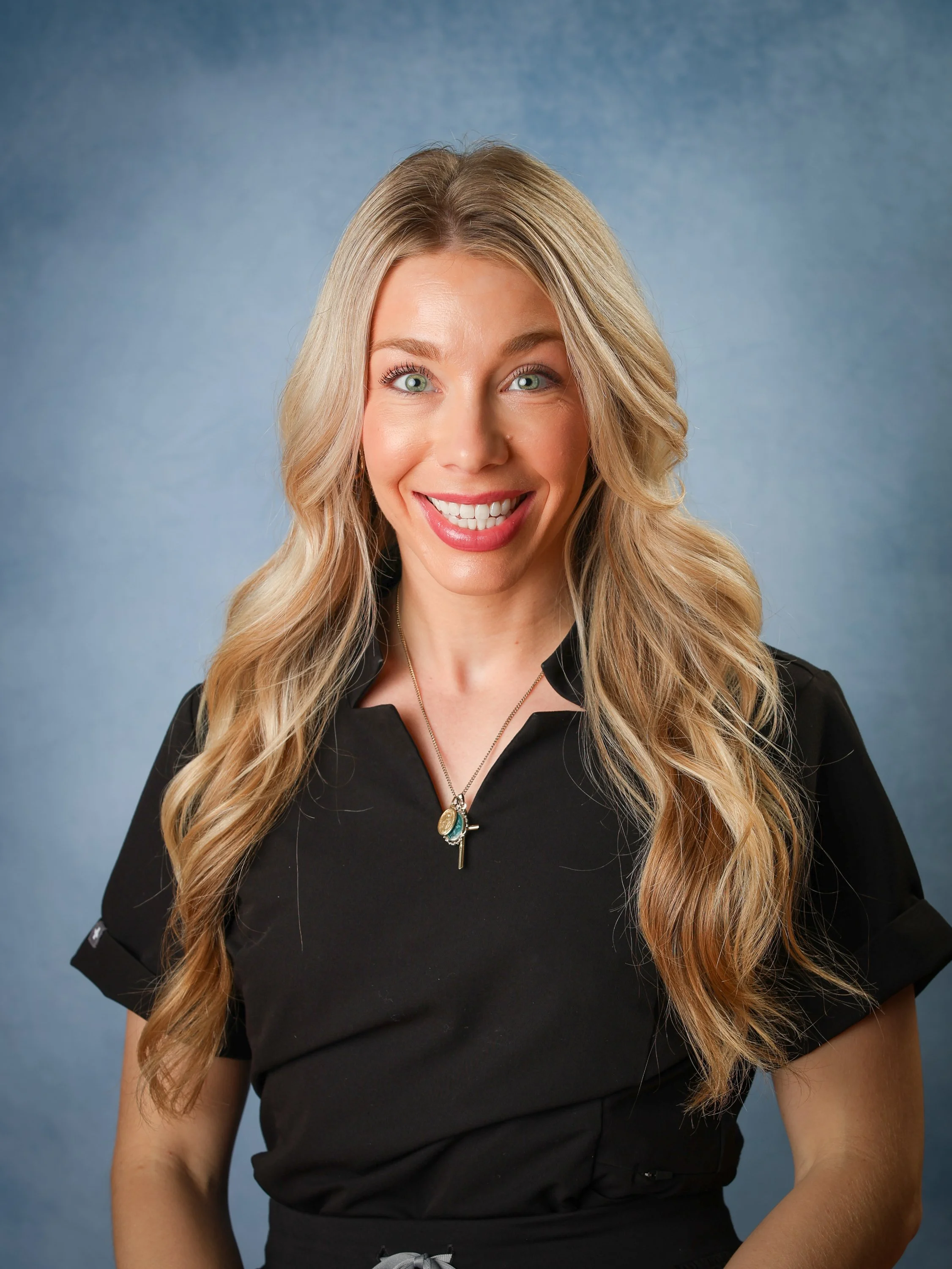 A woman with long blonde hair smiling at the camera with a blue background.