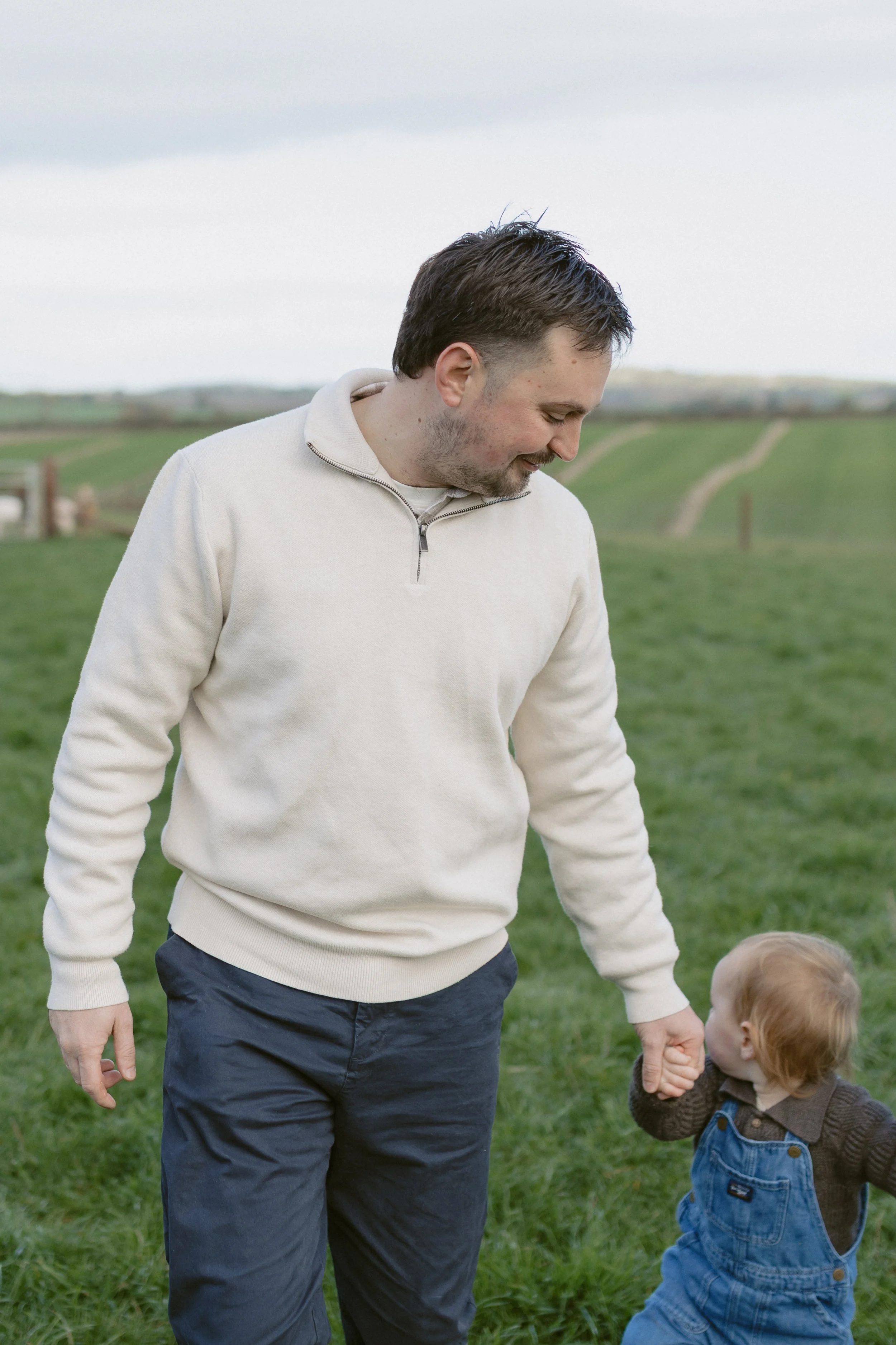 A man holding the hand of a young child in a green field.