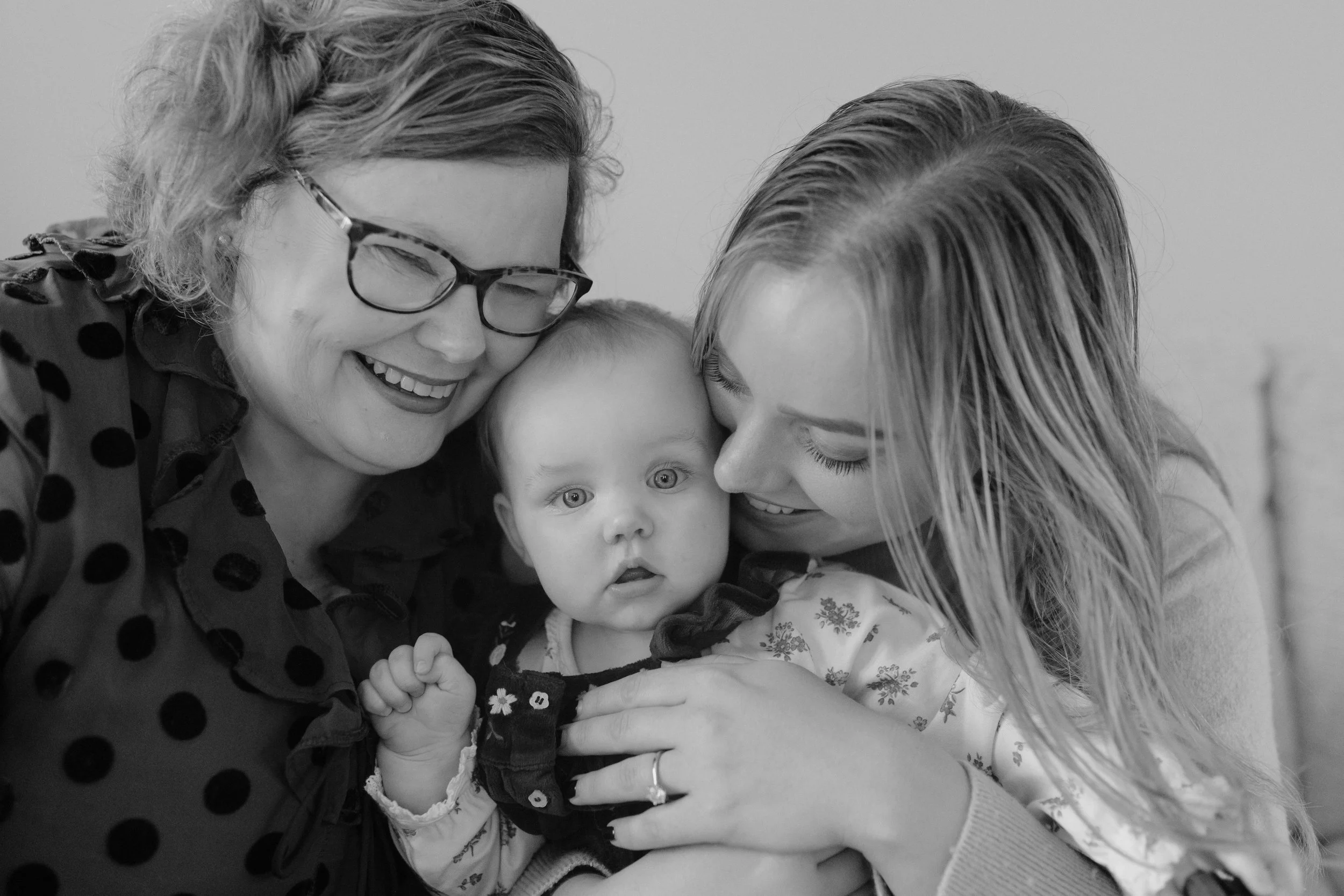 Three generations of women, including a baby, sharing a close, joyful moment together, black and white photograph.
