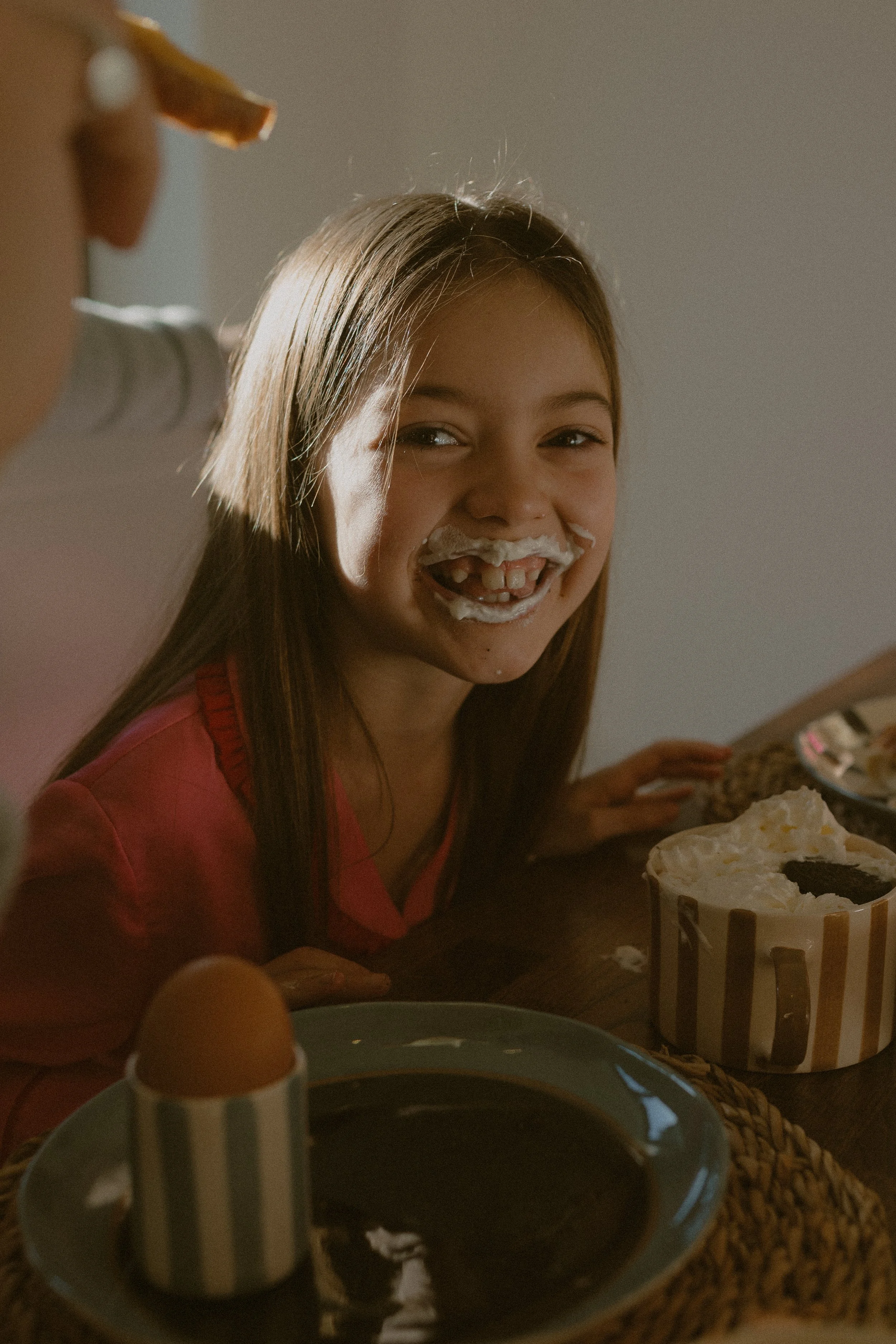 A young girl with cake and icing on her face smiling at the camera during dessert.
