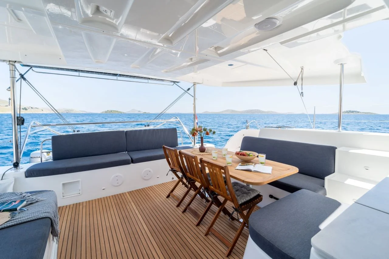 Sitzbereich auf einem Yachtdeck mit Tisch, Stühlen und Blick auf das Meer und Inseln im Hintergrund