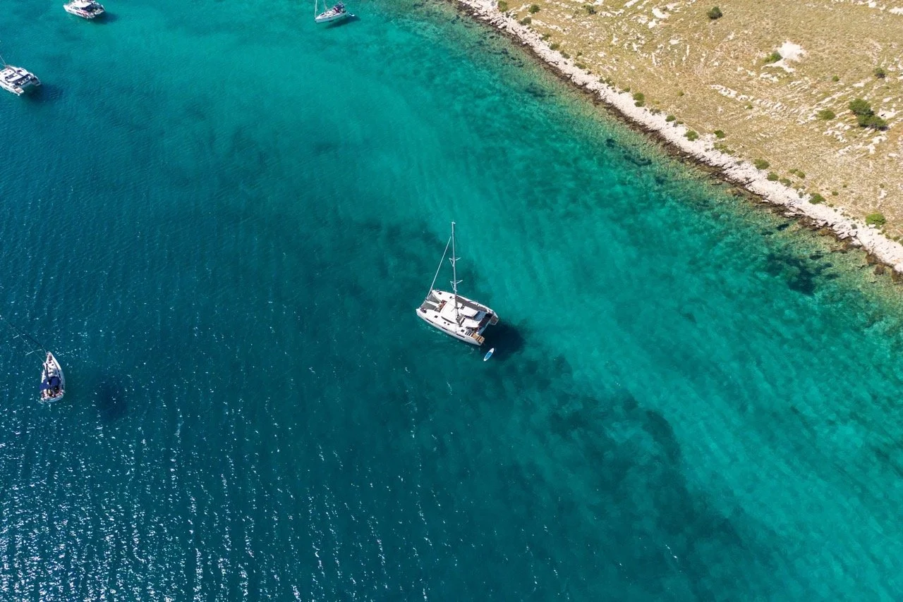 Ein Segelboot liegt in klarem, türkisem Wasser nahe der Küste, umgeben von mehreren kleineren Booten im Hafen.