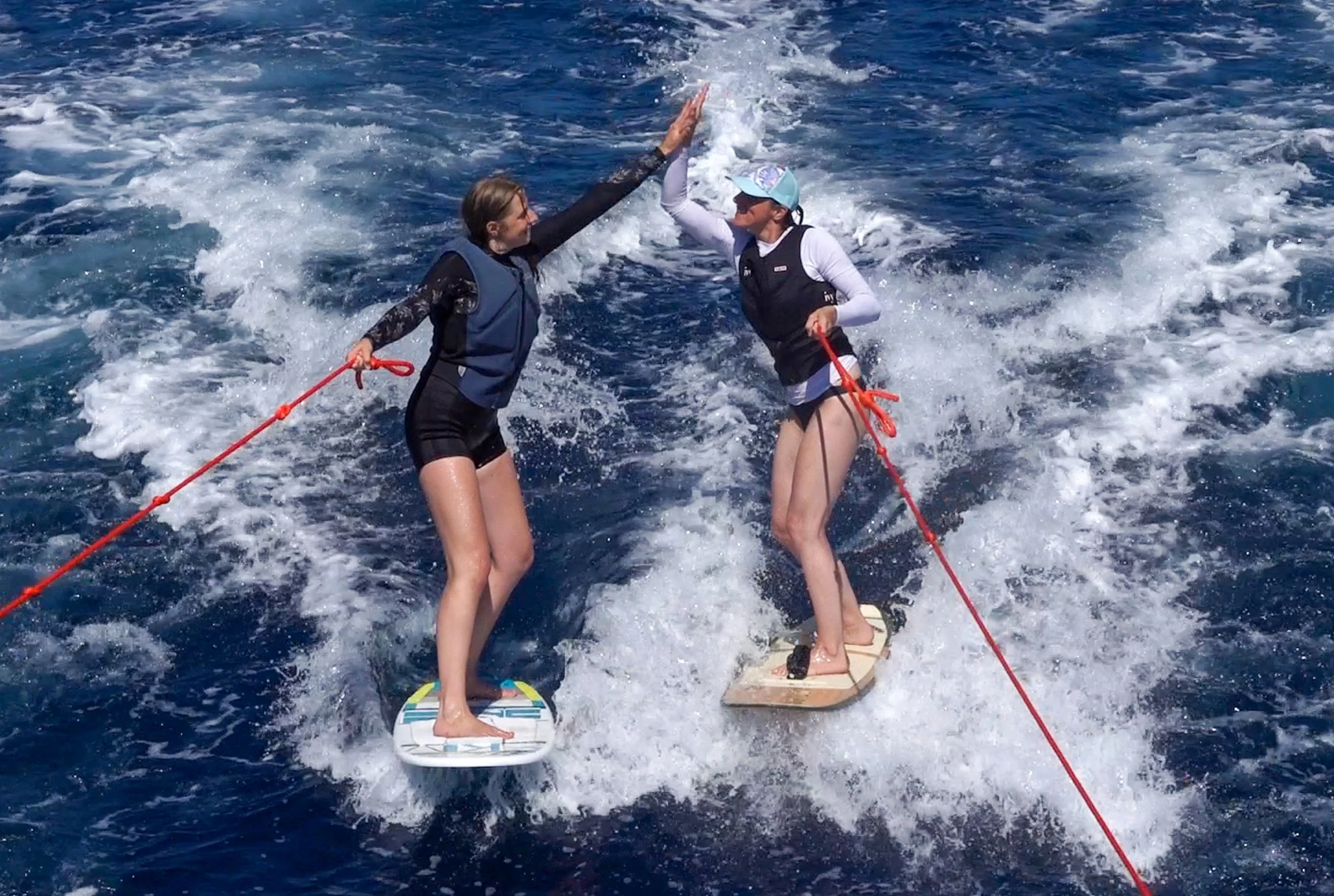 Zwei Frauen surfen auf Wasserbrettern, die sich berühren, während sie auf dem Meer segeln.