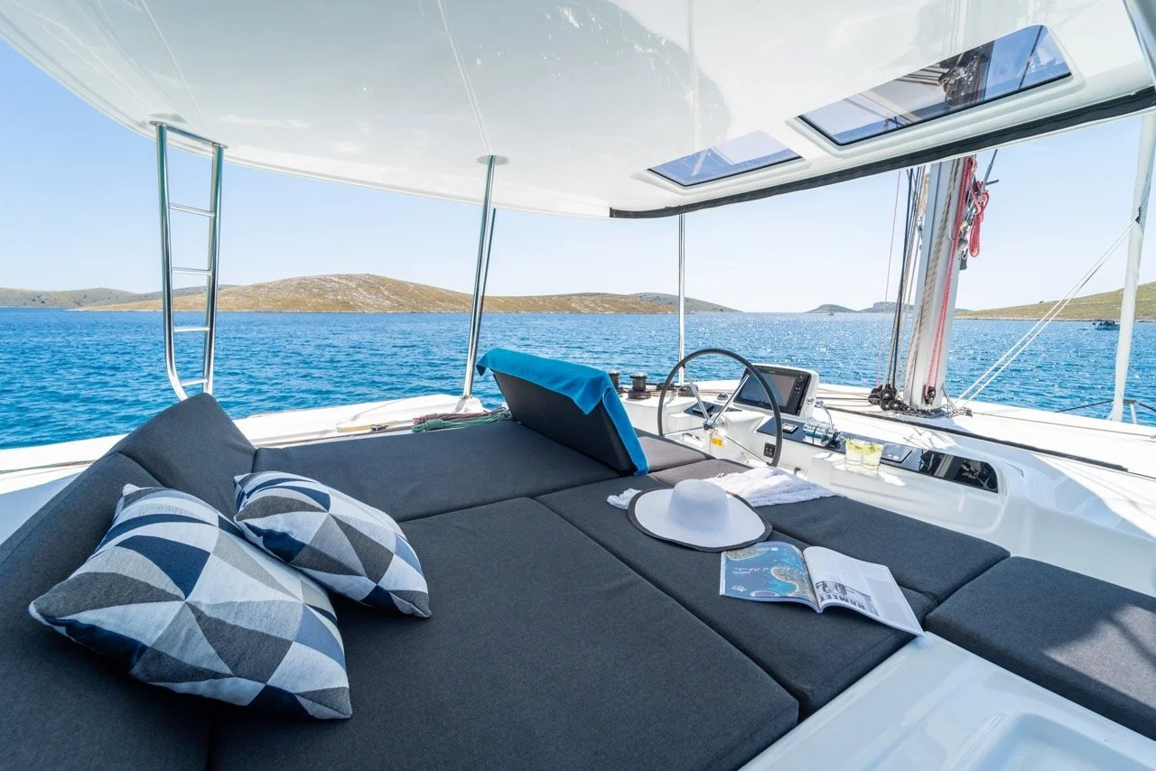 Innenansicht eines Segelboots mit Blick aufs offene Wasser, drei geometrisch gemusterte Kissen, Sonnenhut, aufgeschlagene Karte, Navigationsgerät, Skylights und Rigg