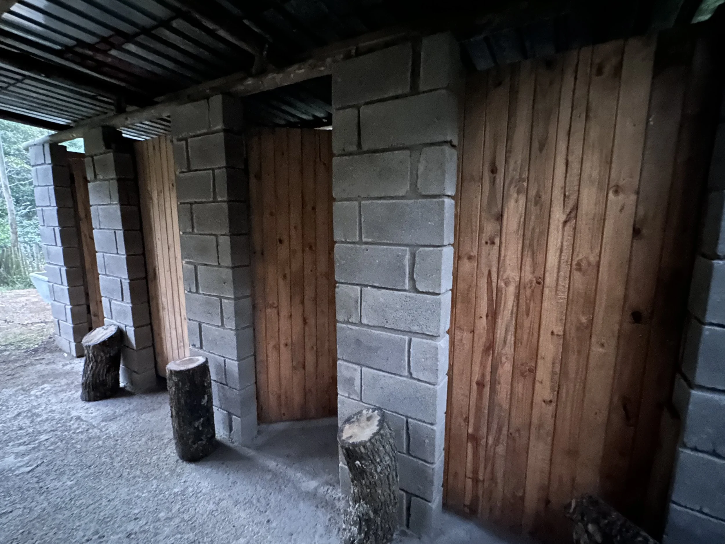 Outdoor cinder block restroom with a toilet and wooden door.